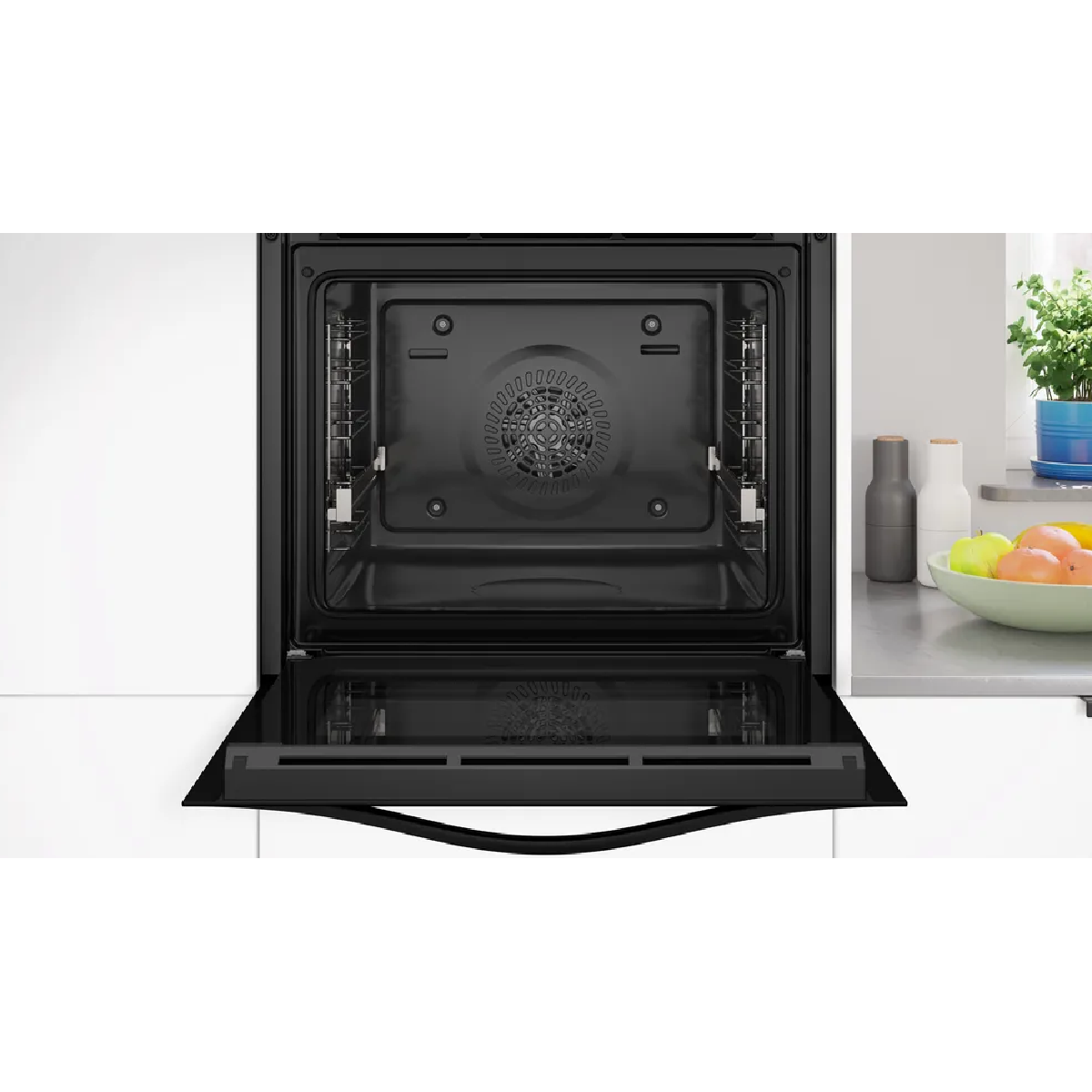Un forno da incasso moderno con porta aperta. A destra frutta e piante.