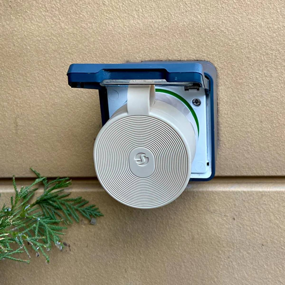 Un enchufe redondo y beige con patrón de espiral está montado en una carcasa azul en una pared.