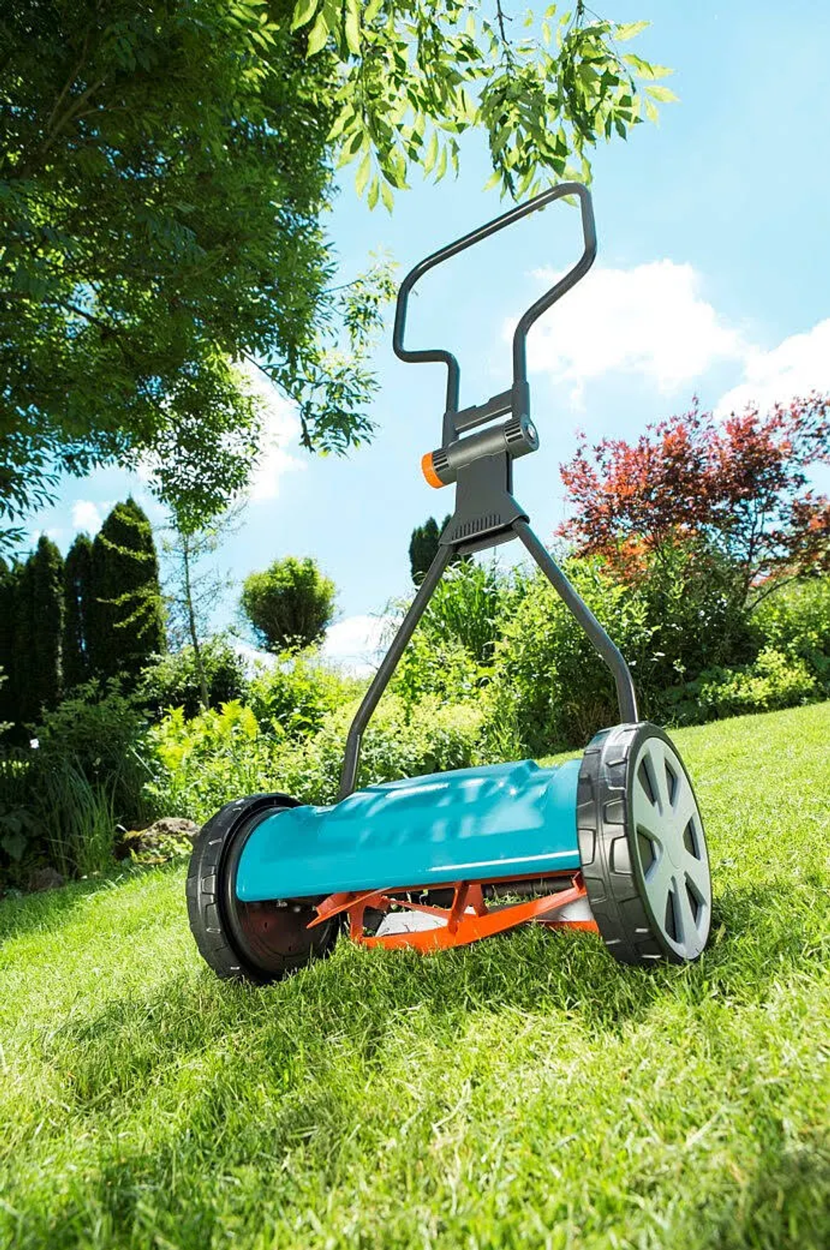 Un cortacésped de carrete turquesa se asienta sobre un césped verde bajo árboles.