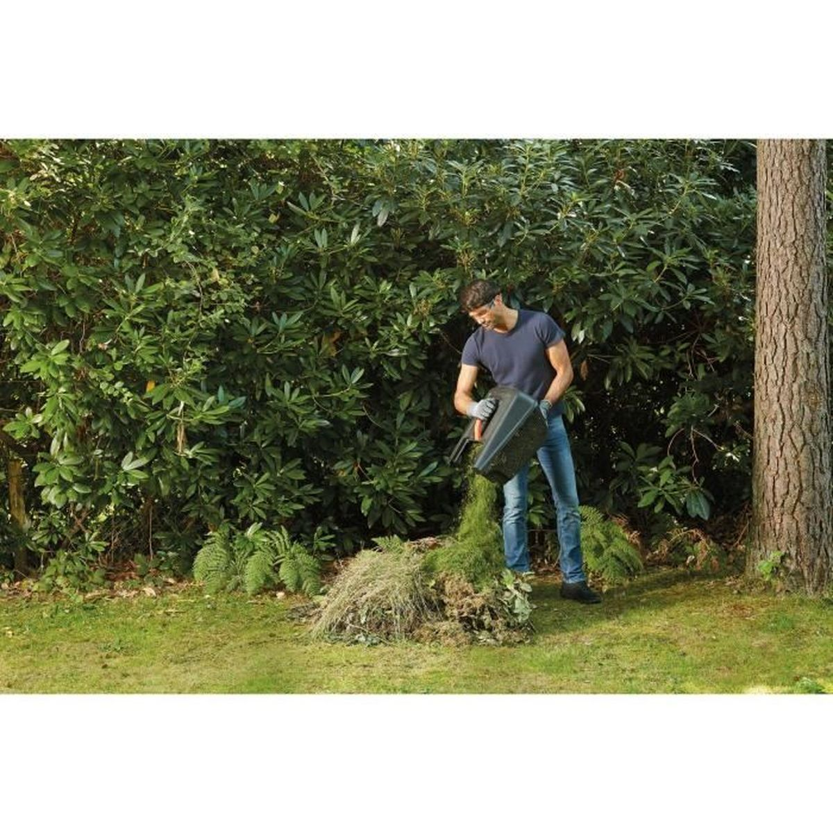 Un hombre con jeans y camiseta azul vierte residuos de jardín de un contenedor sobre un montón.