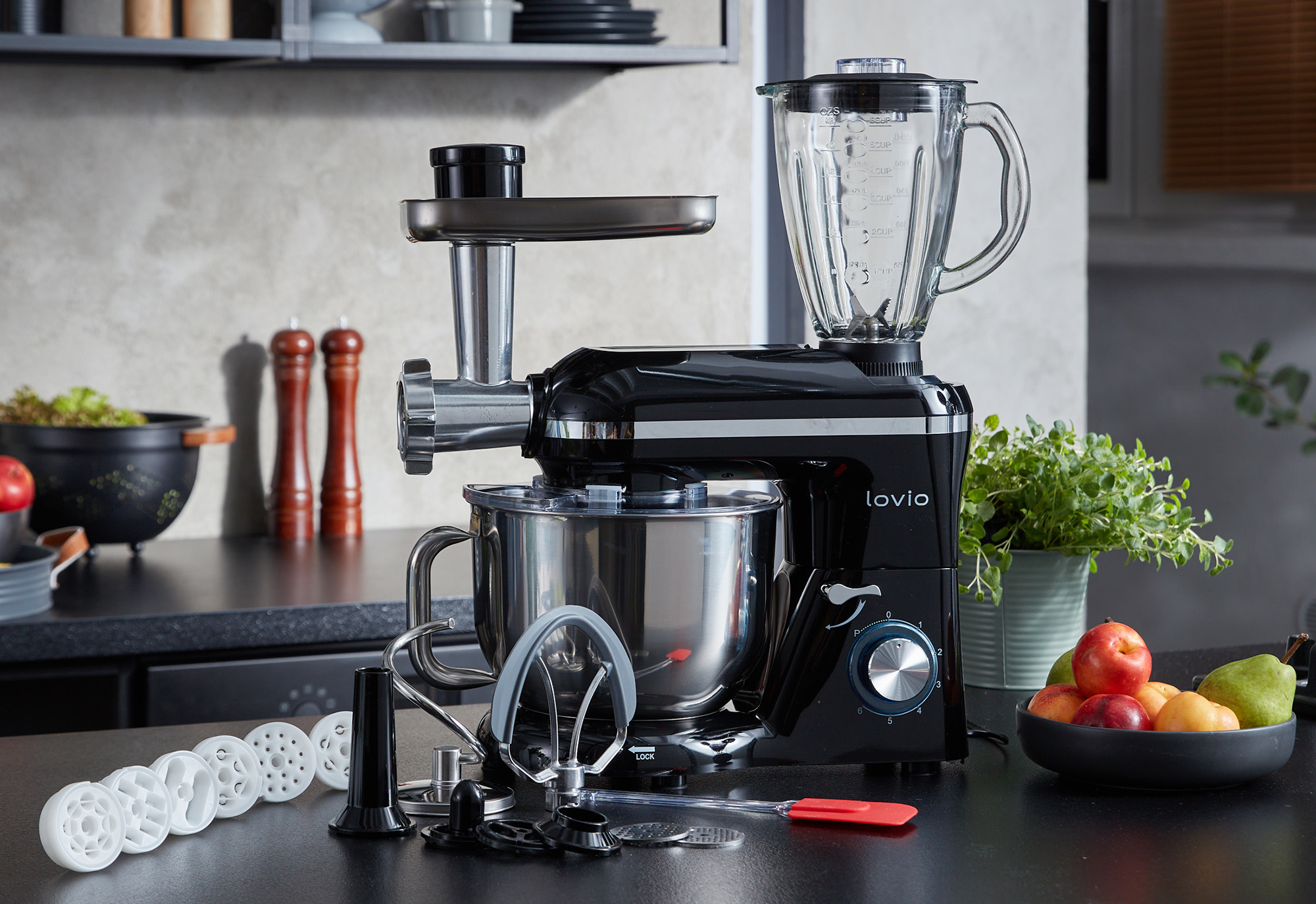 Czarny robot kuchenny z przystawką do mięsa i blenderem, obok owoce.
