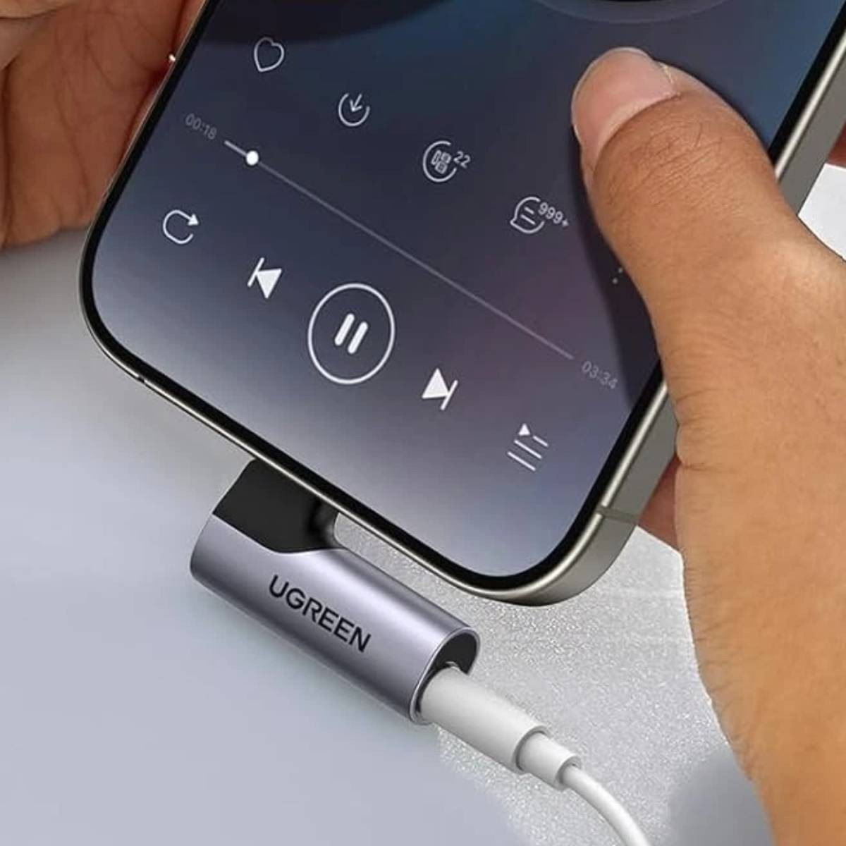 Un adattatore UGREEN collega uno smartphone a un cavo audio. Un dito controlla la riproduzione musicale.