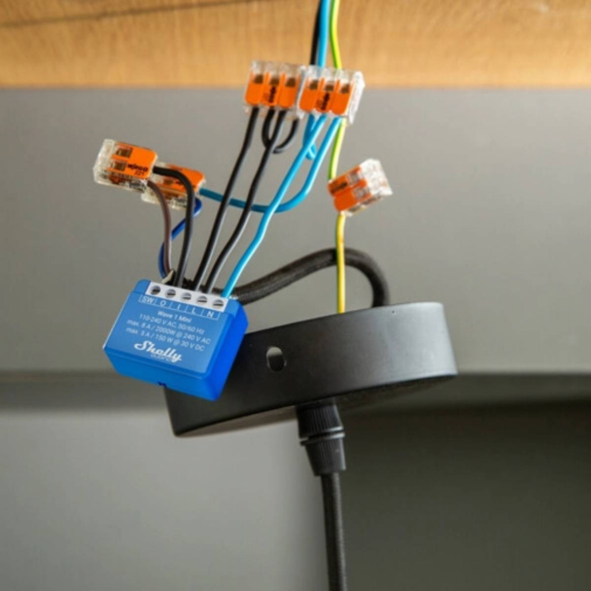 Un interruttore Shelly blu con cavi e connettori arancioni pende da un supporto a soffitto.