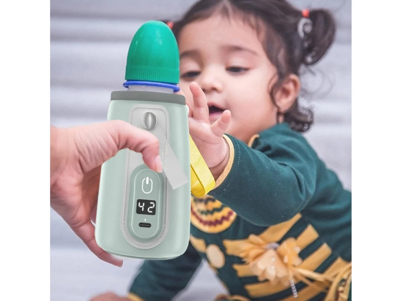 Eine Hand hält eine mintgrüne Flasche mit grünem Deckel. Ein Baby im Hintergrund greift danach.