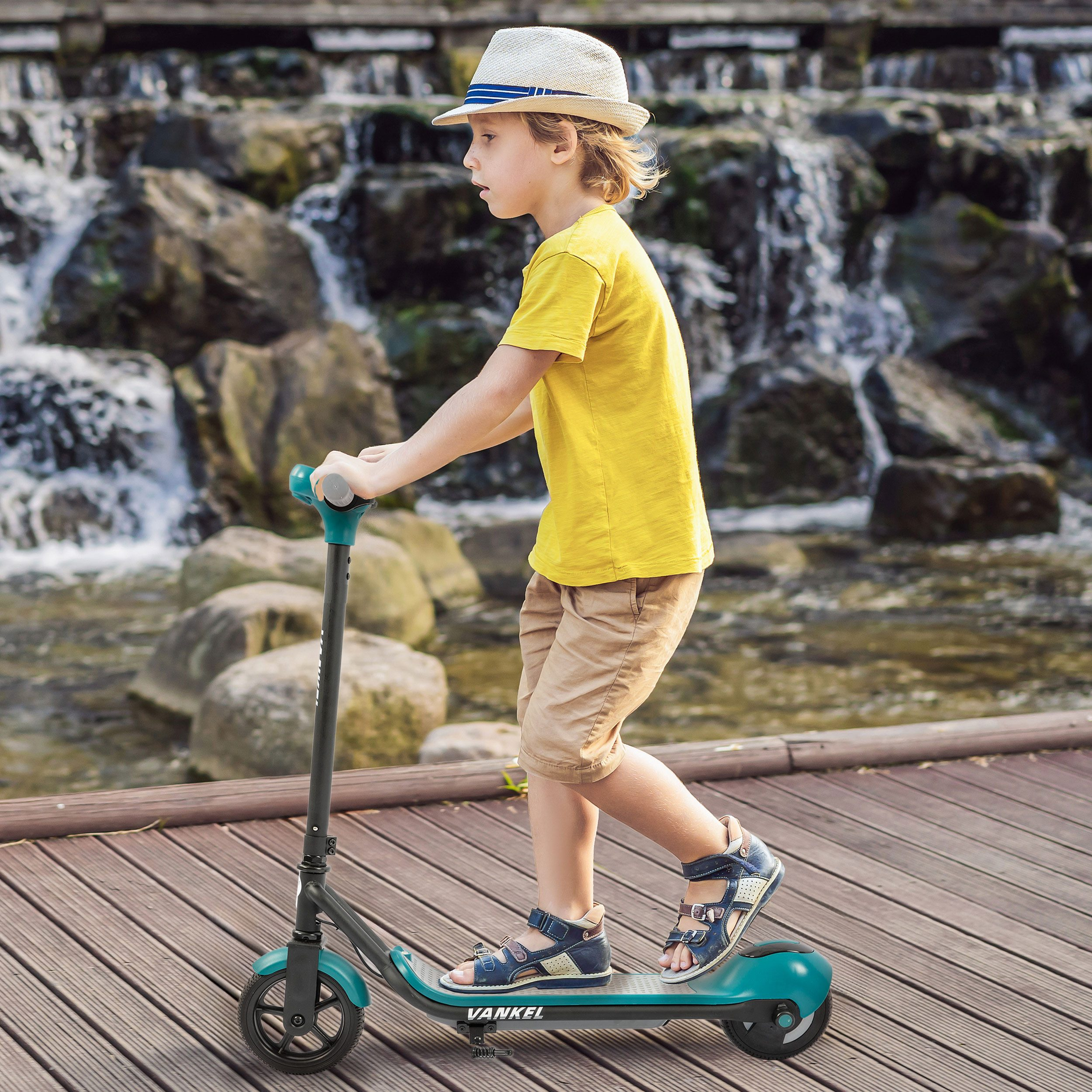 Ein Junge in einem gelben Hemd und Hut fährt auf einem Roller über eine Holzplanke vor einem Wasserfall.