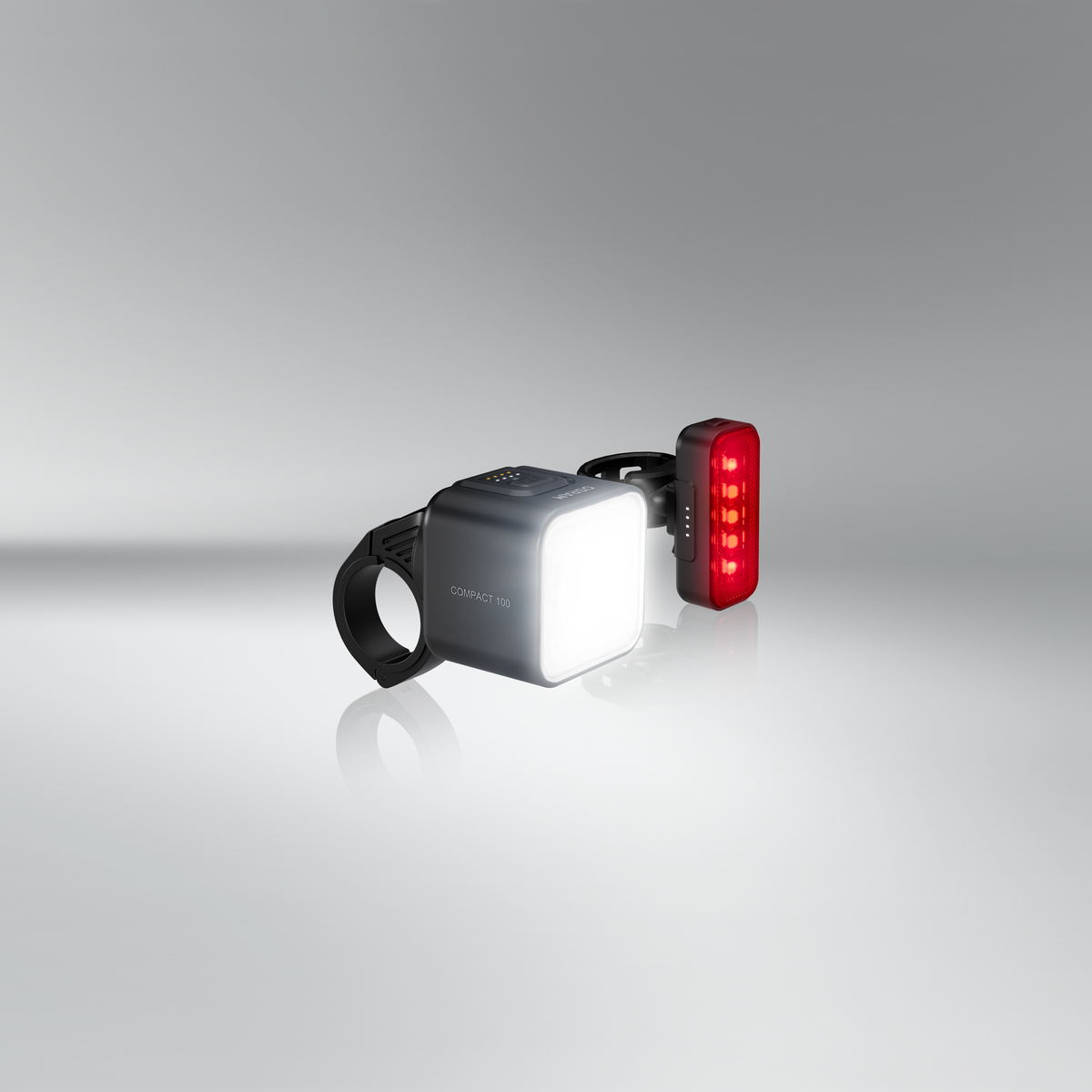 Grauer Würfel-Scheinwerfer und rotes Rücklicht für Fahrräder, auf grauem Hintergrund.