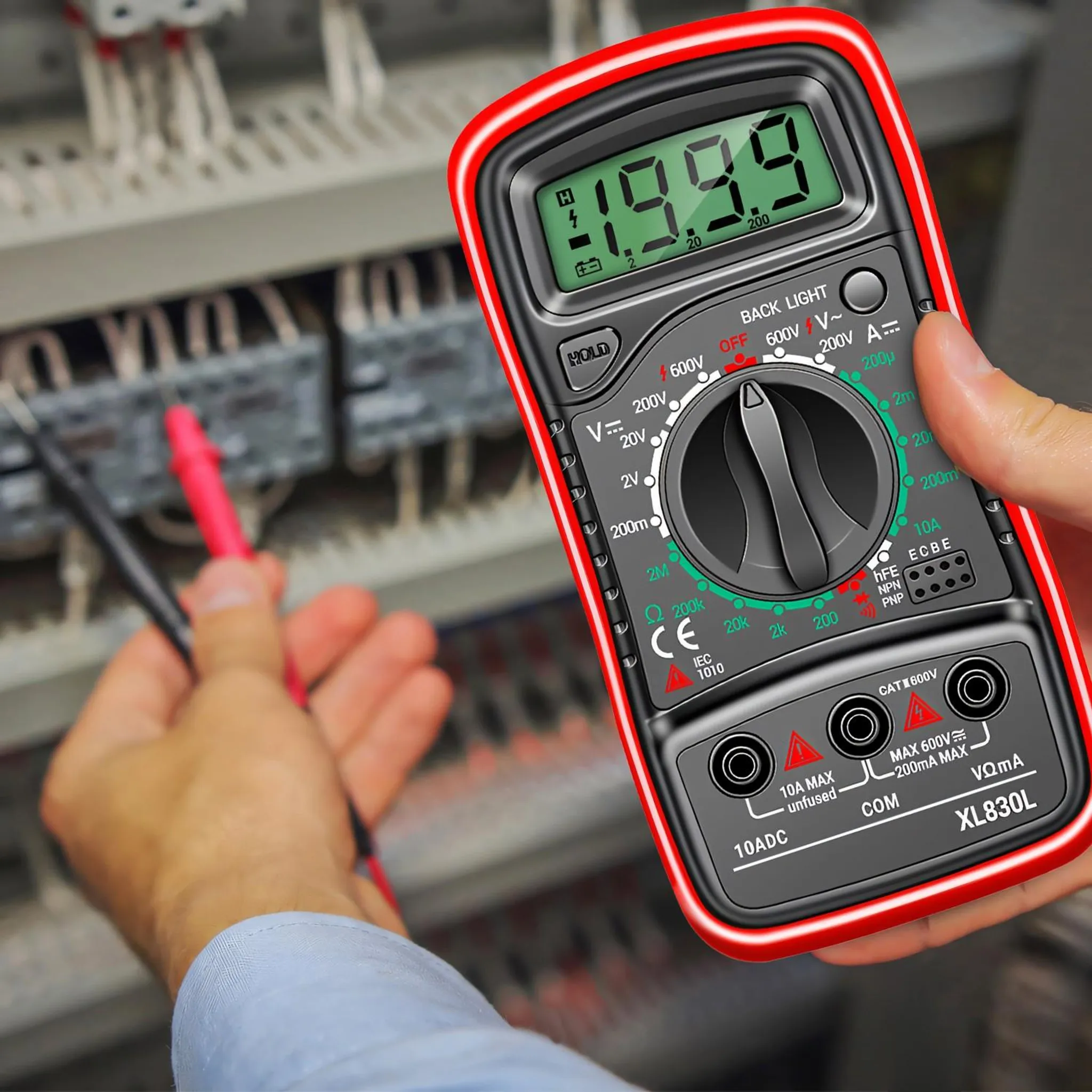 Eine Hand hält ein rotes Digitalmultimeter in der Nähe von elektrischen Leitungen und Schalttafeln.