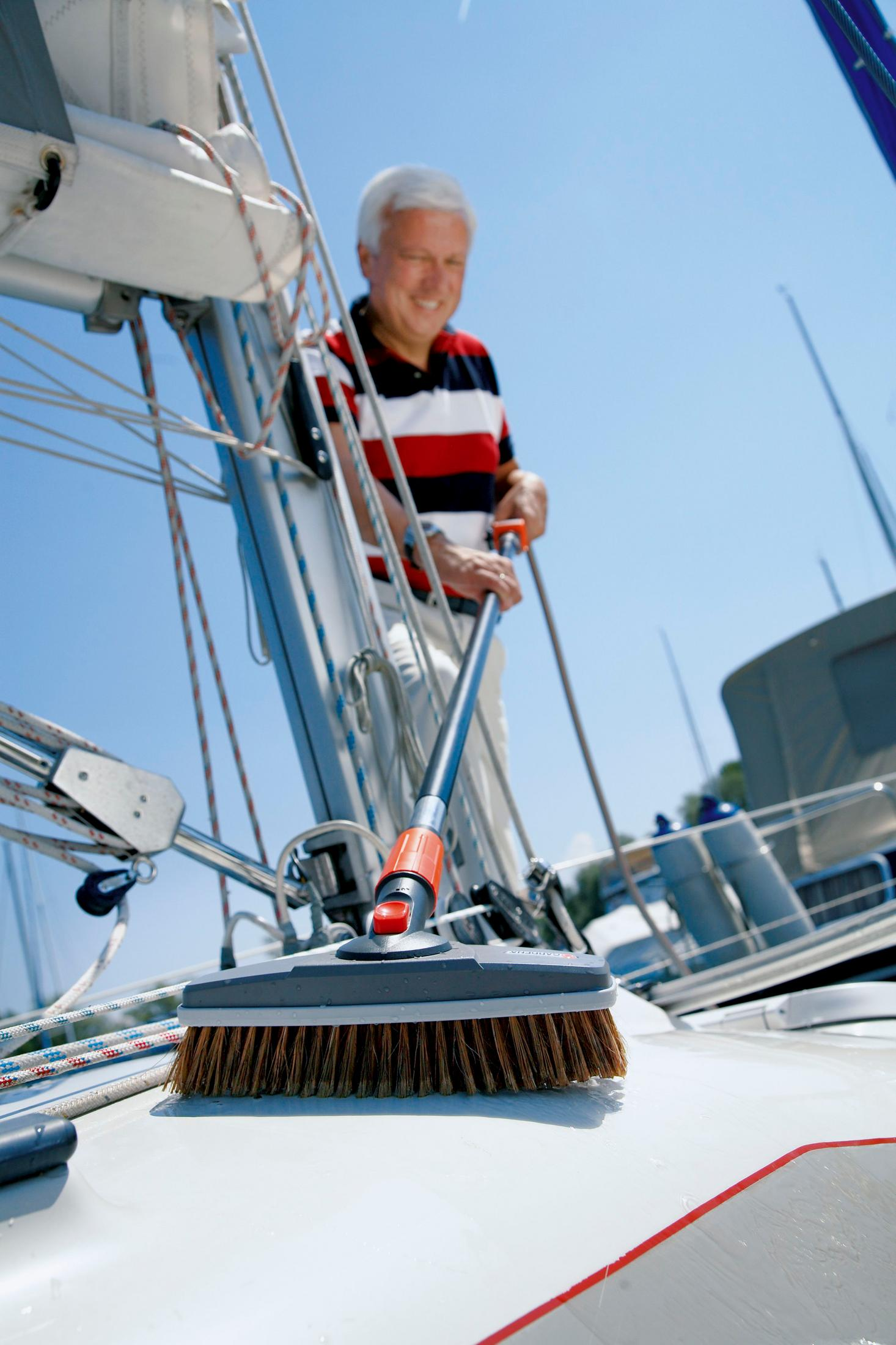 Uomo con capelli bianchi che pulisce una barca a vela con una spazzola.