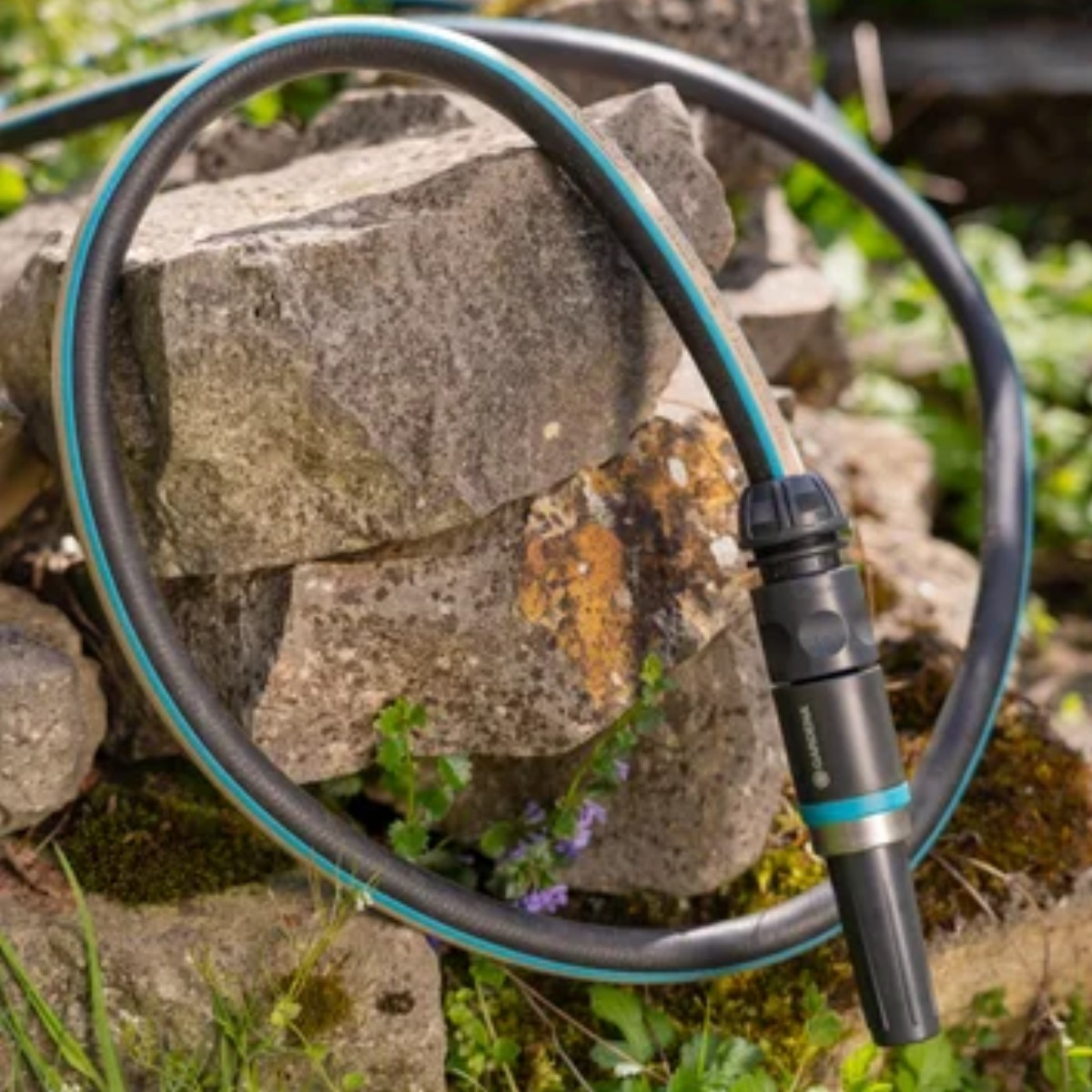 Un tubo da giardino nero con strisce blu drappeggiato su rocce.