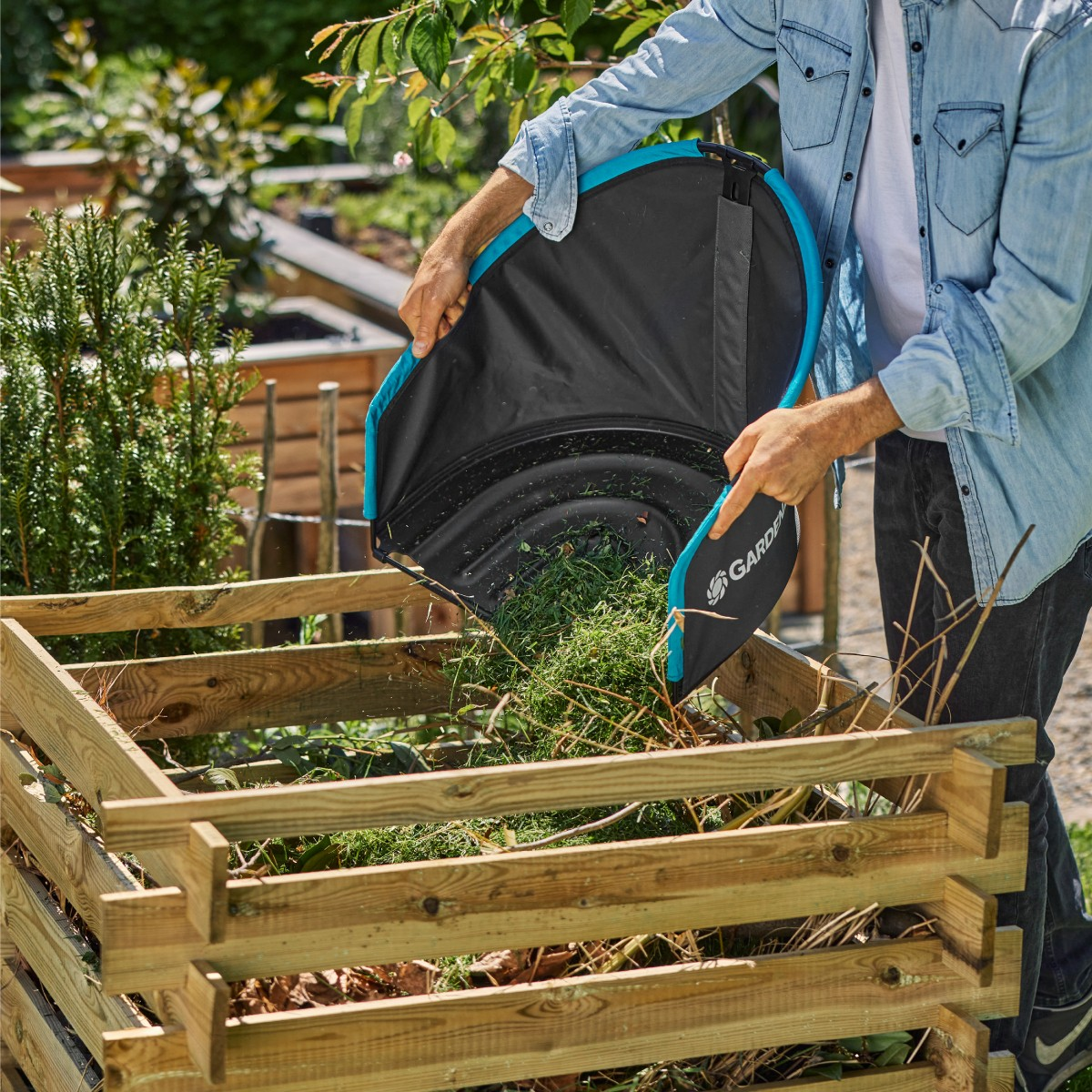 Uomo svuota erba tagliata con sacca Gardena nera in un composter di legno.