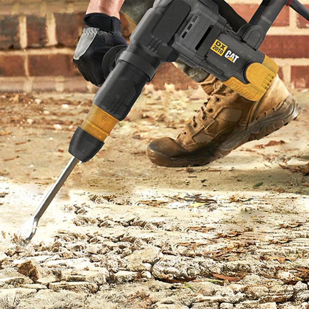 Bir kırıcı beton kırıyor. Eldivenli el aleti tutuyor, bot yakında duruyor.