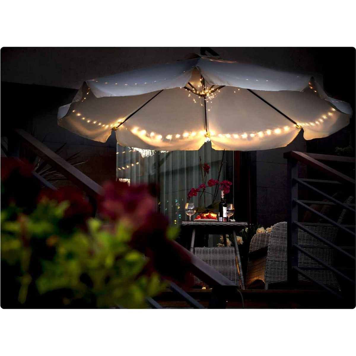 Un ombrellone bianco con lucine illumina un tavolo con vino e bicchieri.