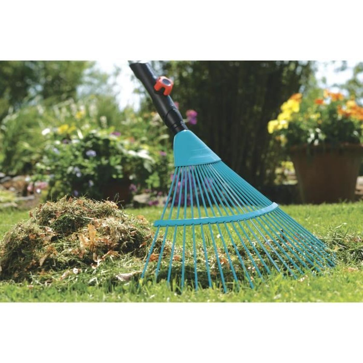 Un rastrello turchese poggia sull'erba accanto a un mucchio di sfalci in un giardino.