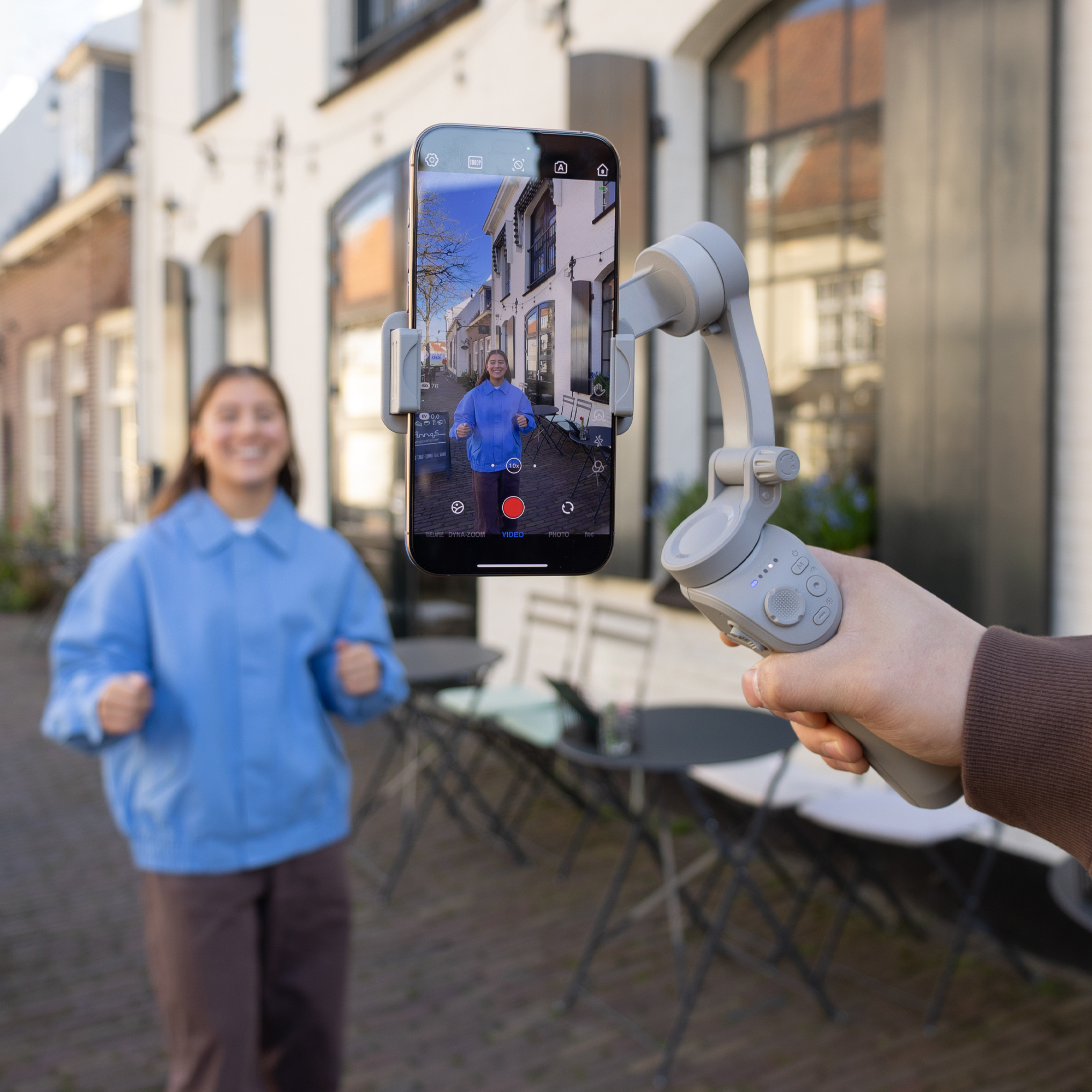 A person holds a gimbal with a smartphone showing a woman.