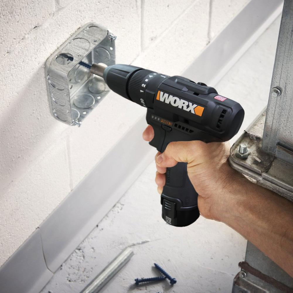 Una mano usa un trapano nero per avvitare in una scatola metallica su un muro bianco.