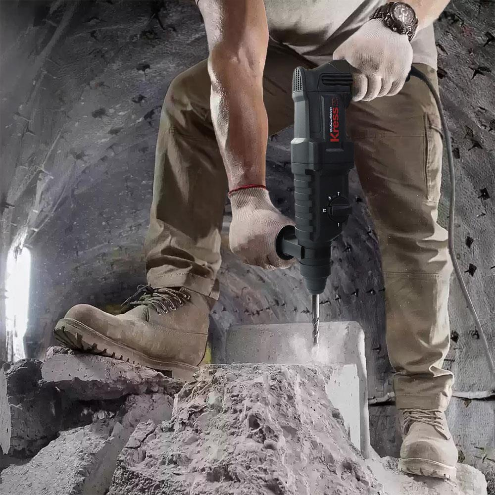 İşçi kıyafetli adam, siyah darbeli matkapla beton bloğu deliyor.