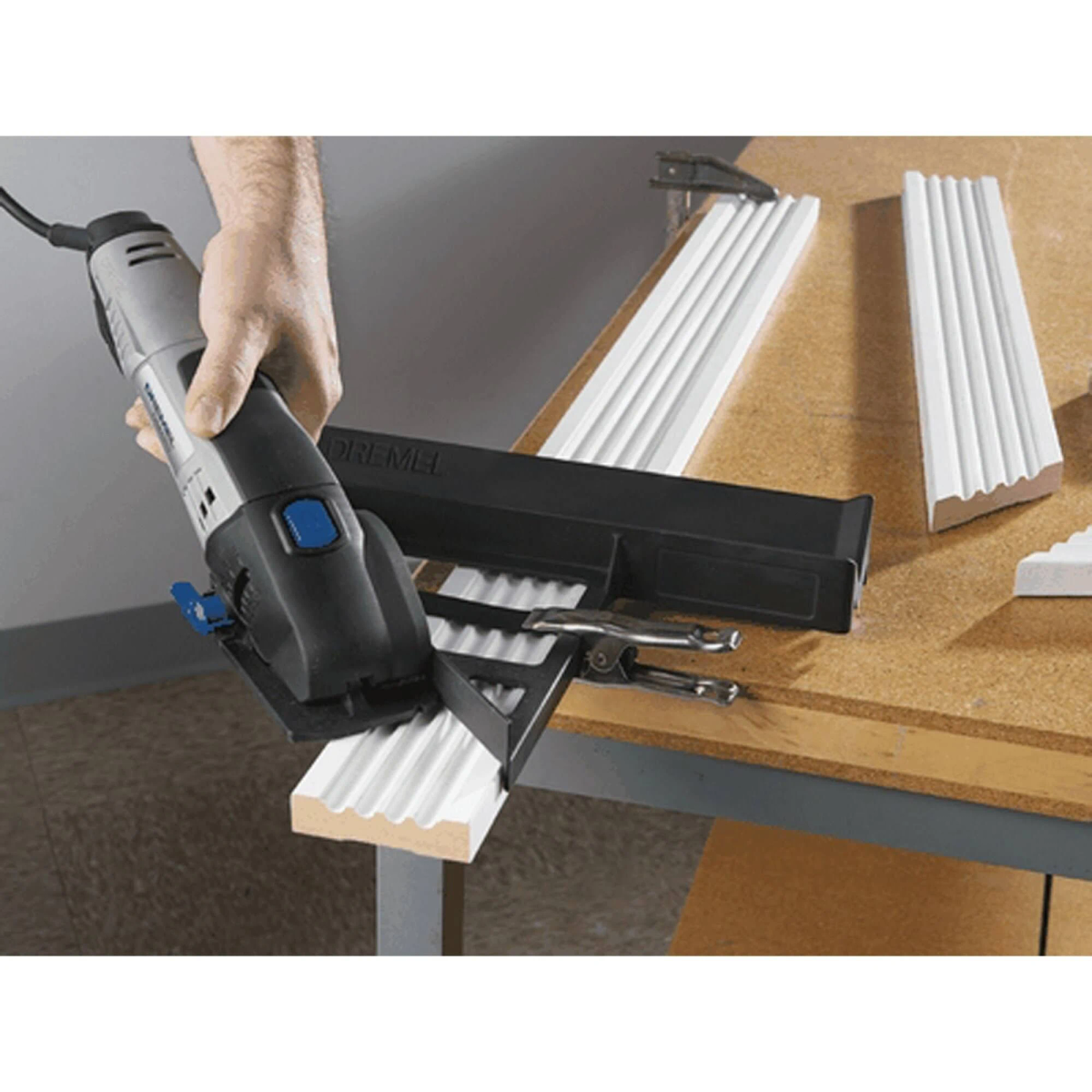 Mano sujetando herramienta Dremel cortando moldura blanca acanalada.