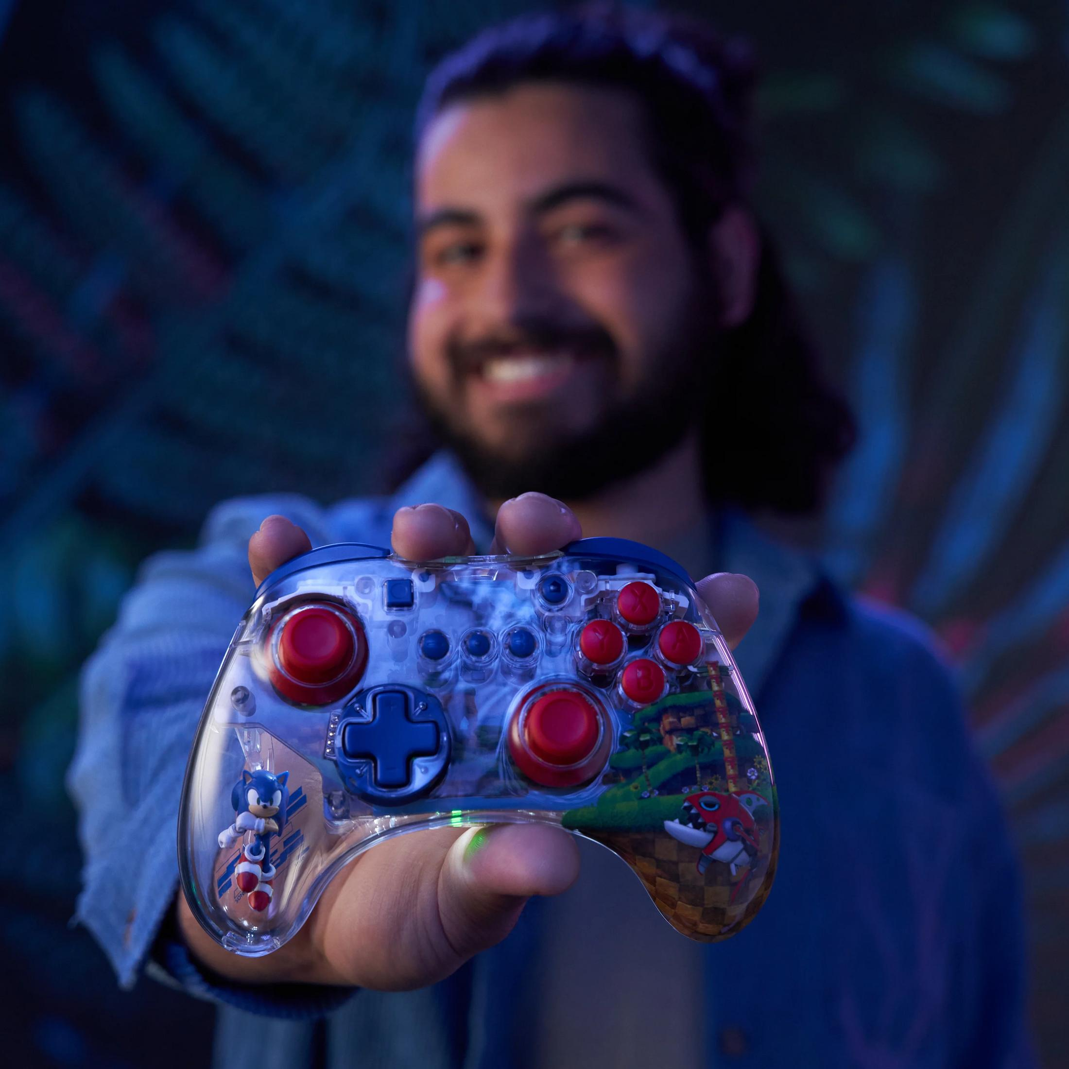 Ein Mann hält einen transparenten Controller mit Sonic-Motiven. Blaue und rote Knöpfe sind sichtbar.