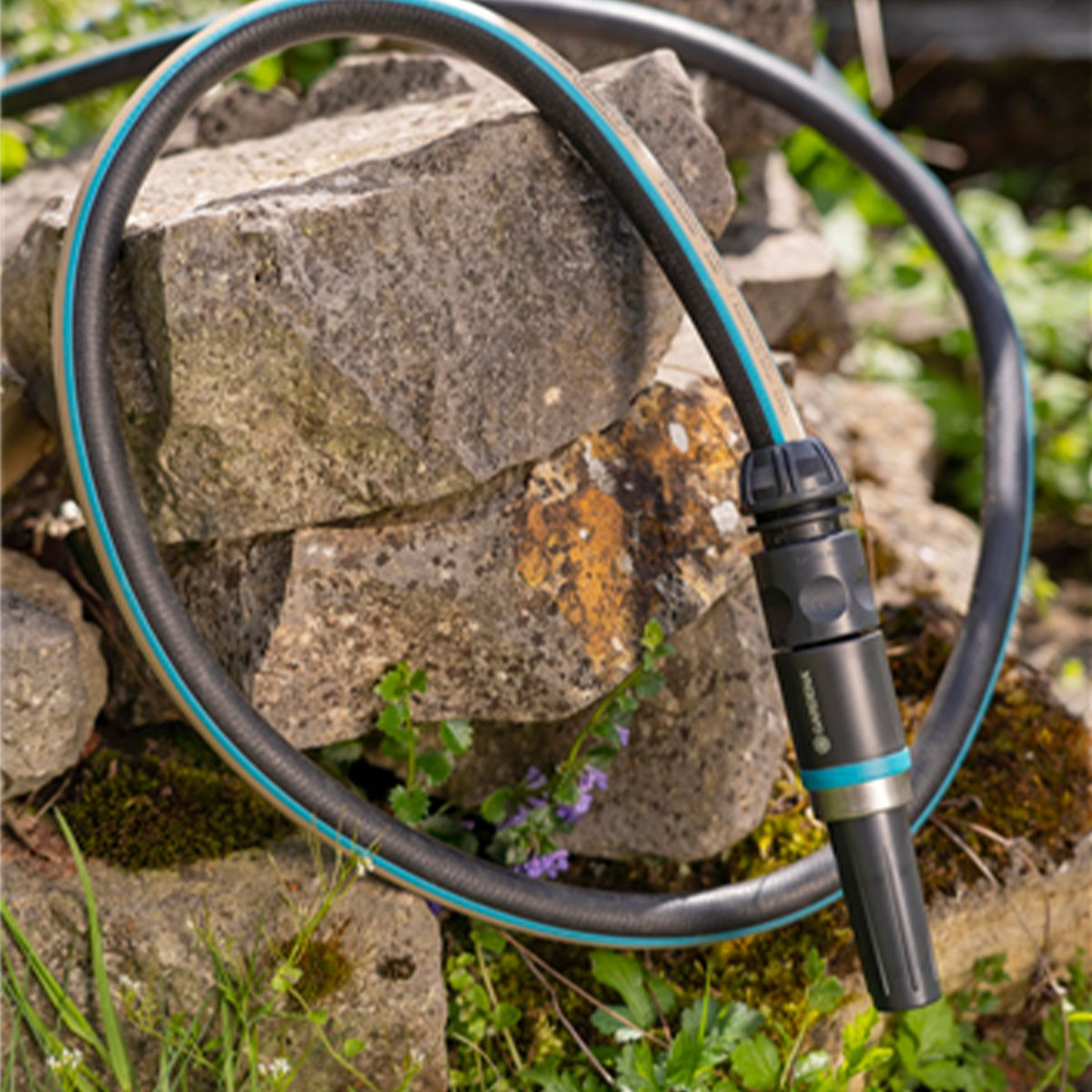 Tubo da giardino nero con striscia blu appoggiato su pietre.