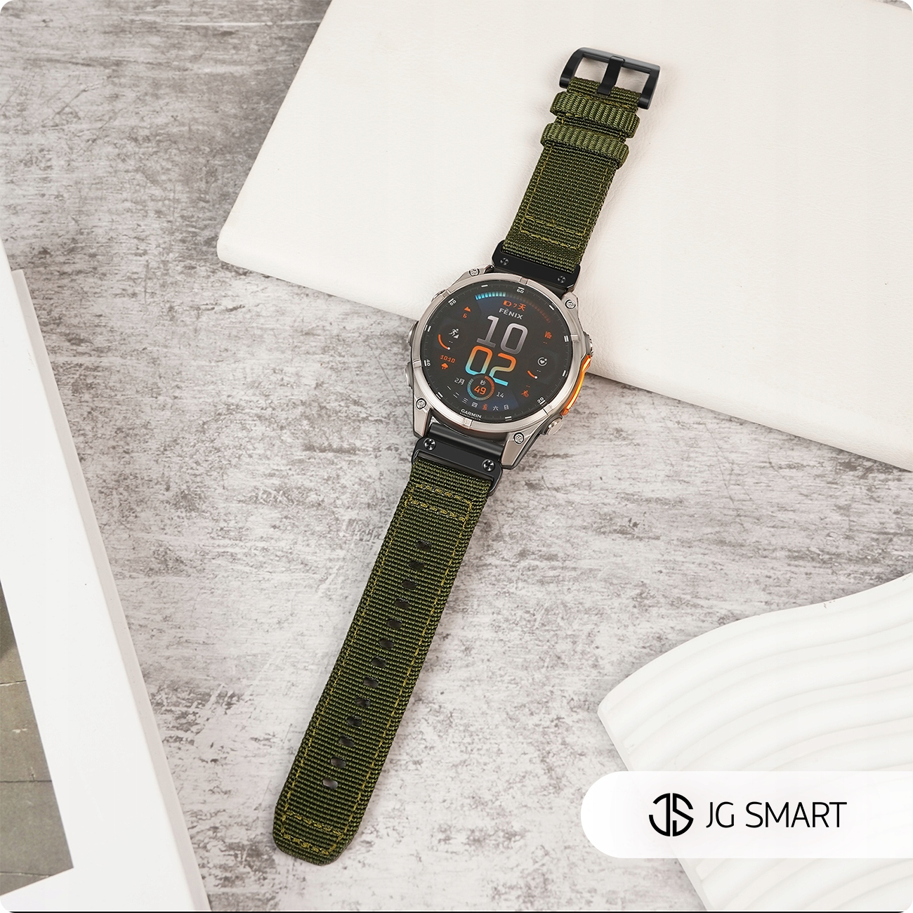 Zegarek Garmin Fenix z zielonym materiałowym paskiem spoczywa na teksturowanej powierzchni.