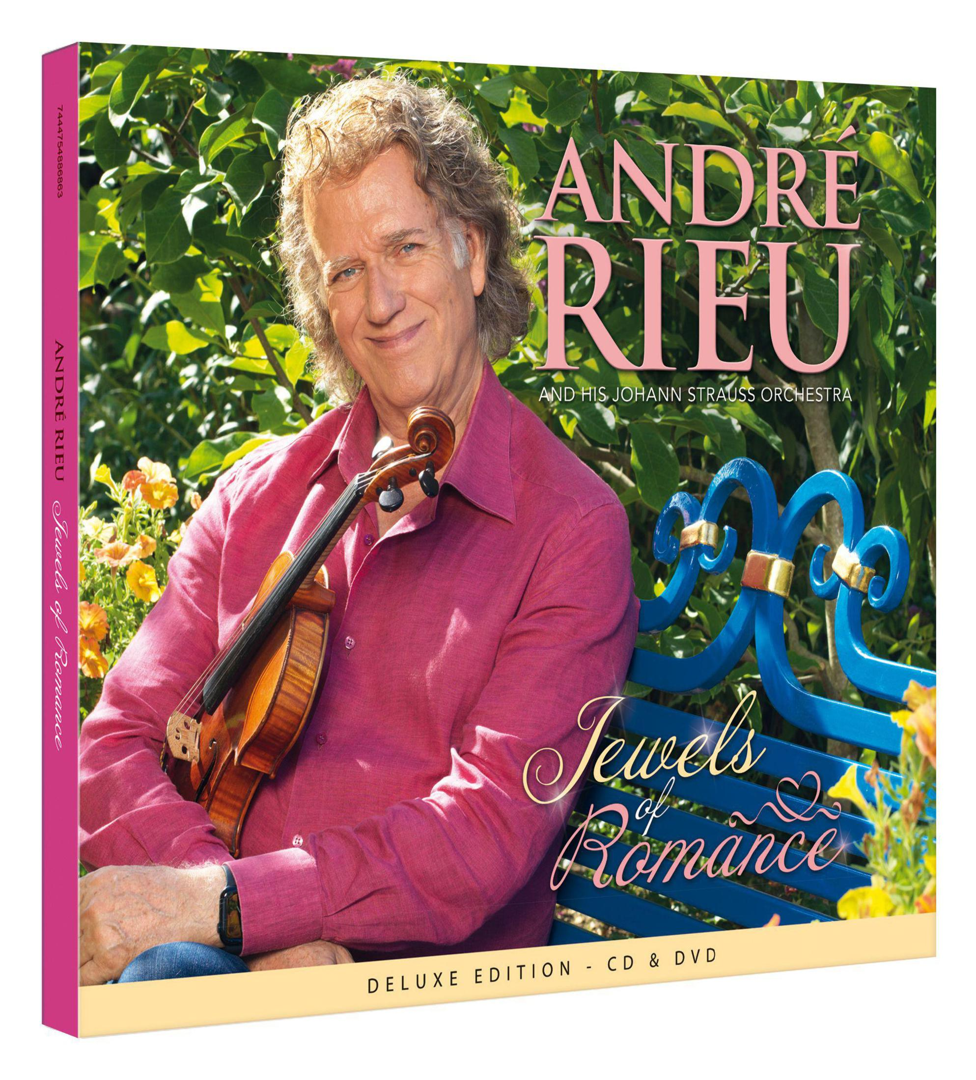 Andre Rieu zit met een viool op een parkbank voor bloeiende sering.