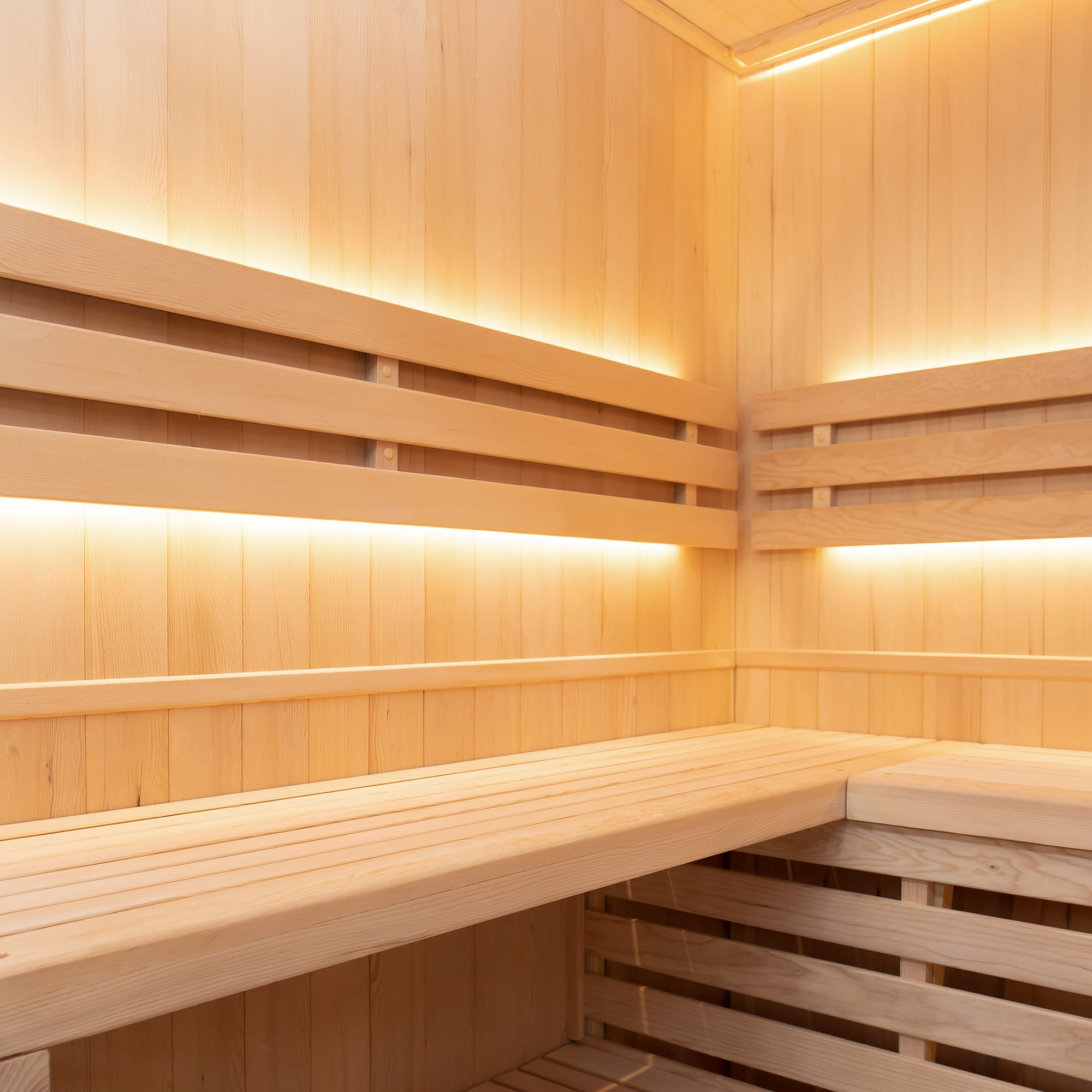 Una sala de sauna de madera con bancos y luz indirecta.