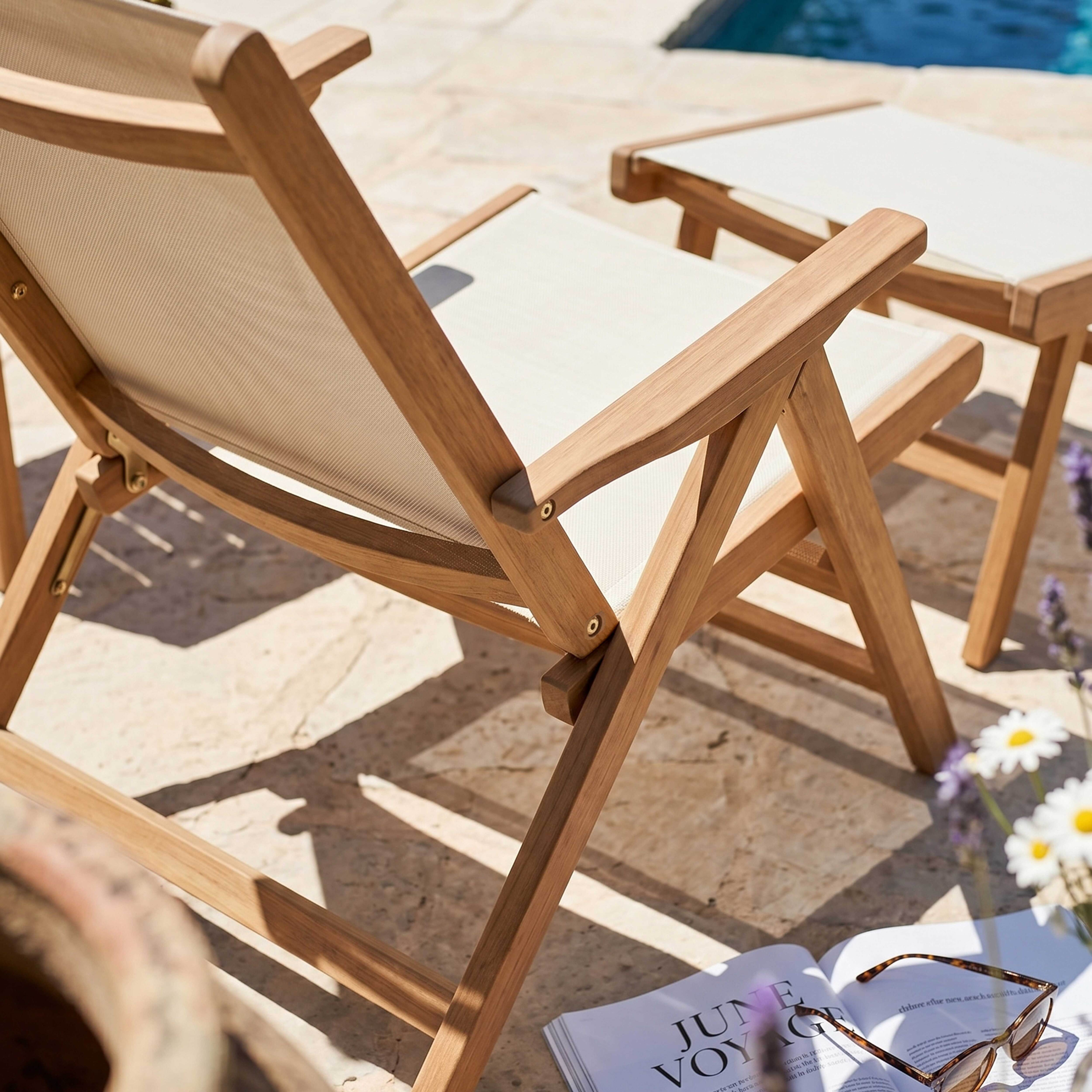 Zwei Holzliegen mit weißen Bezügen stehen auf Steinplatten nahe einem Pool.