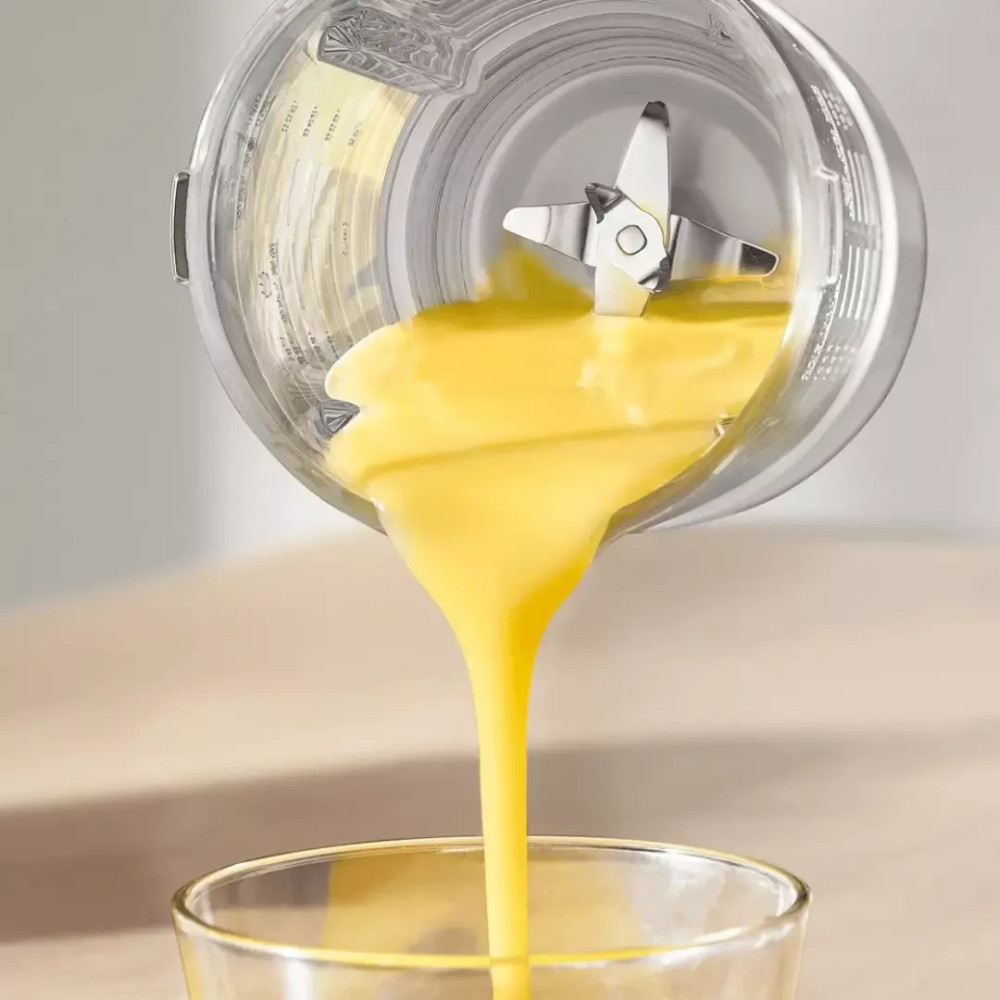 Liquido giallo versa da un bicchiere frullatore in un bicchiere.