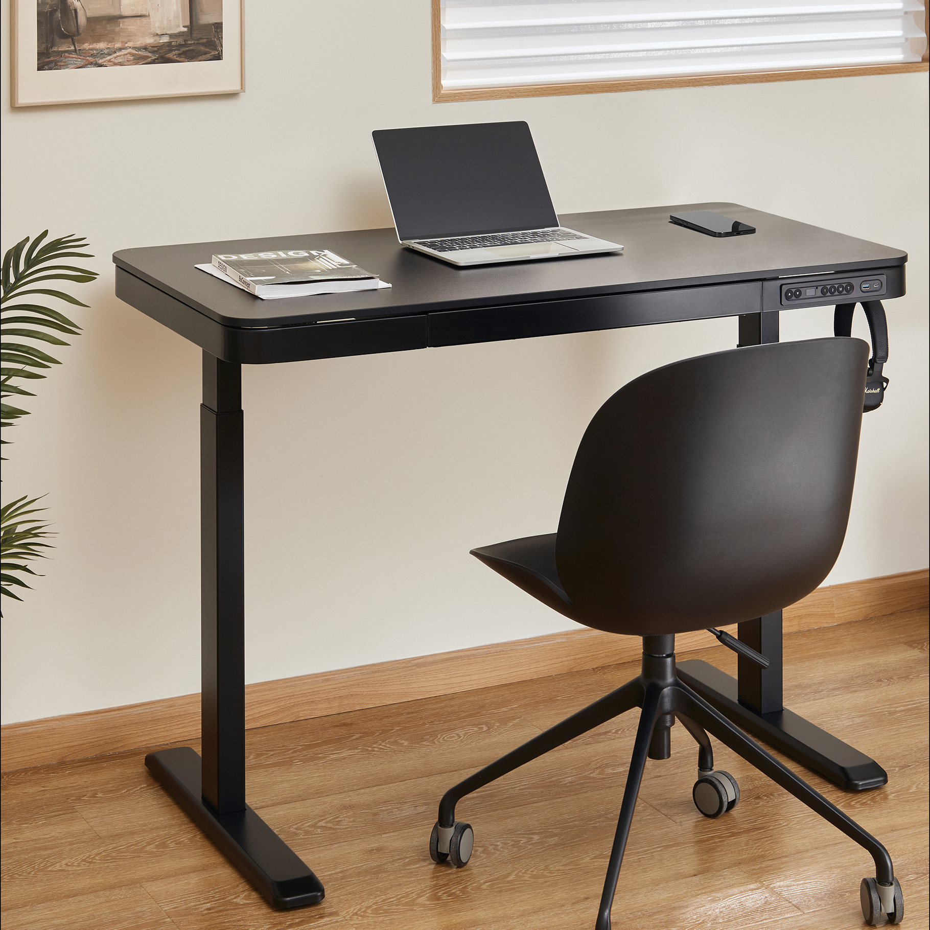 Escritorio negro con portátil, teléfono y una silla de oficina negra al lado.