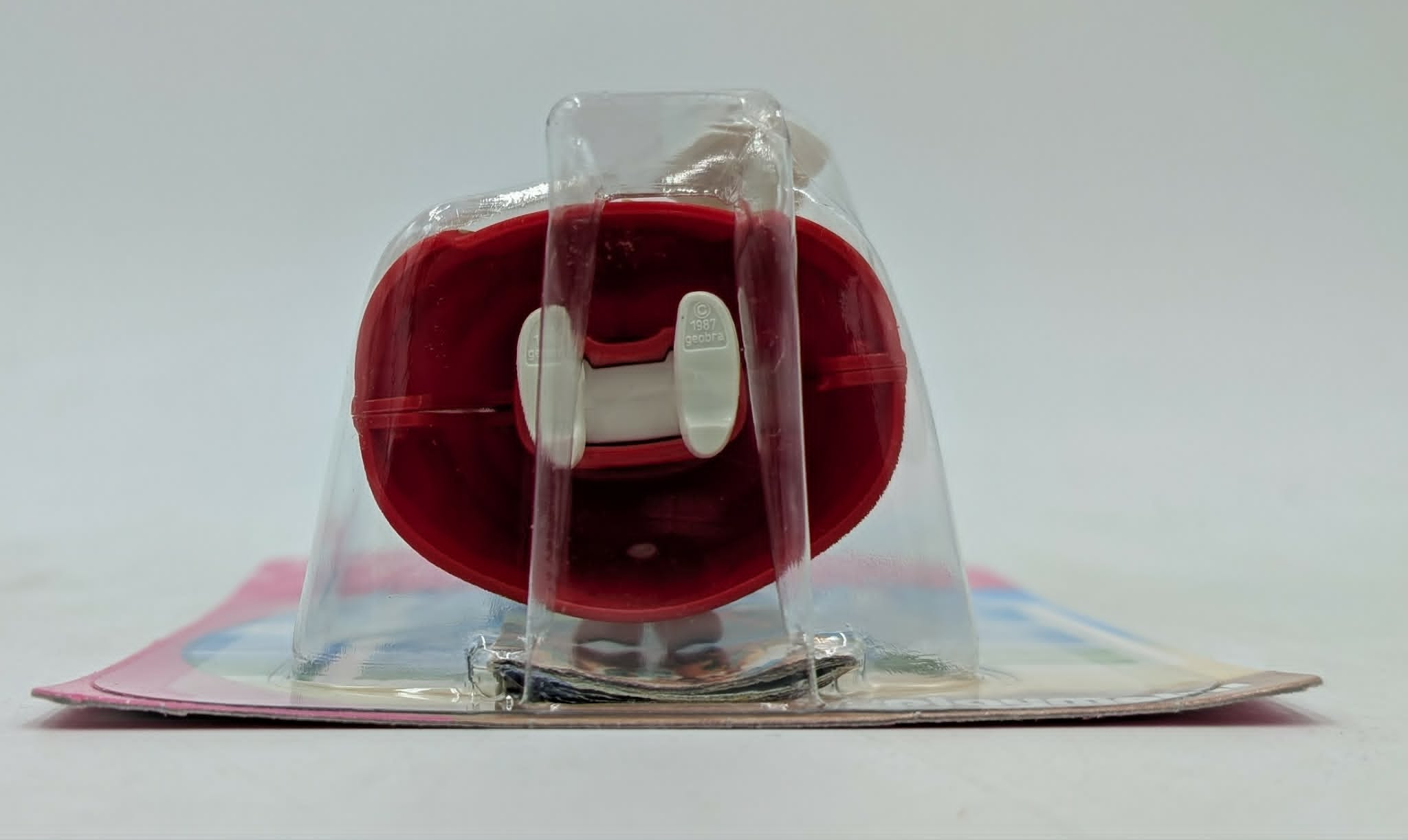 Un oggetto rosso in confezione di plastica, con fermagli bianchi.