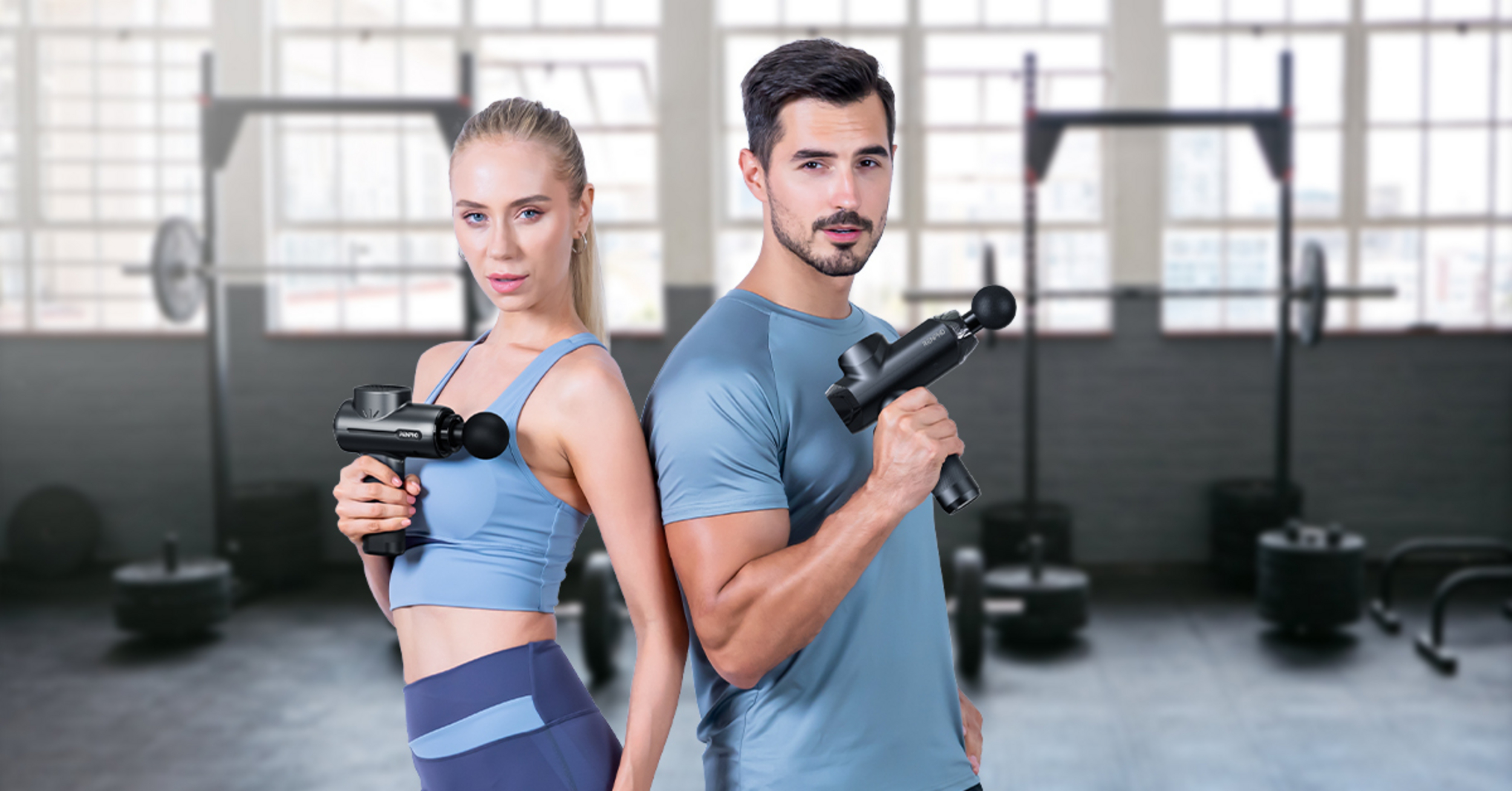 Mann und Frau mit Massagepistolen in einem Fitnessstudio mit Gewichten.