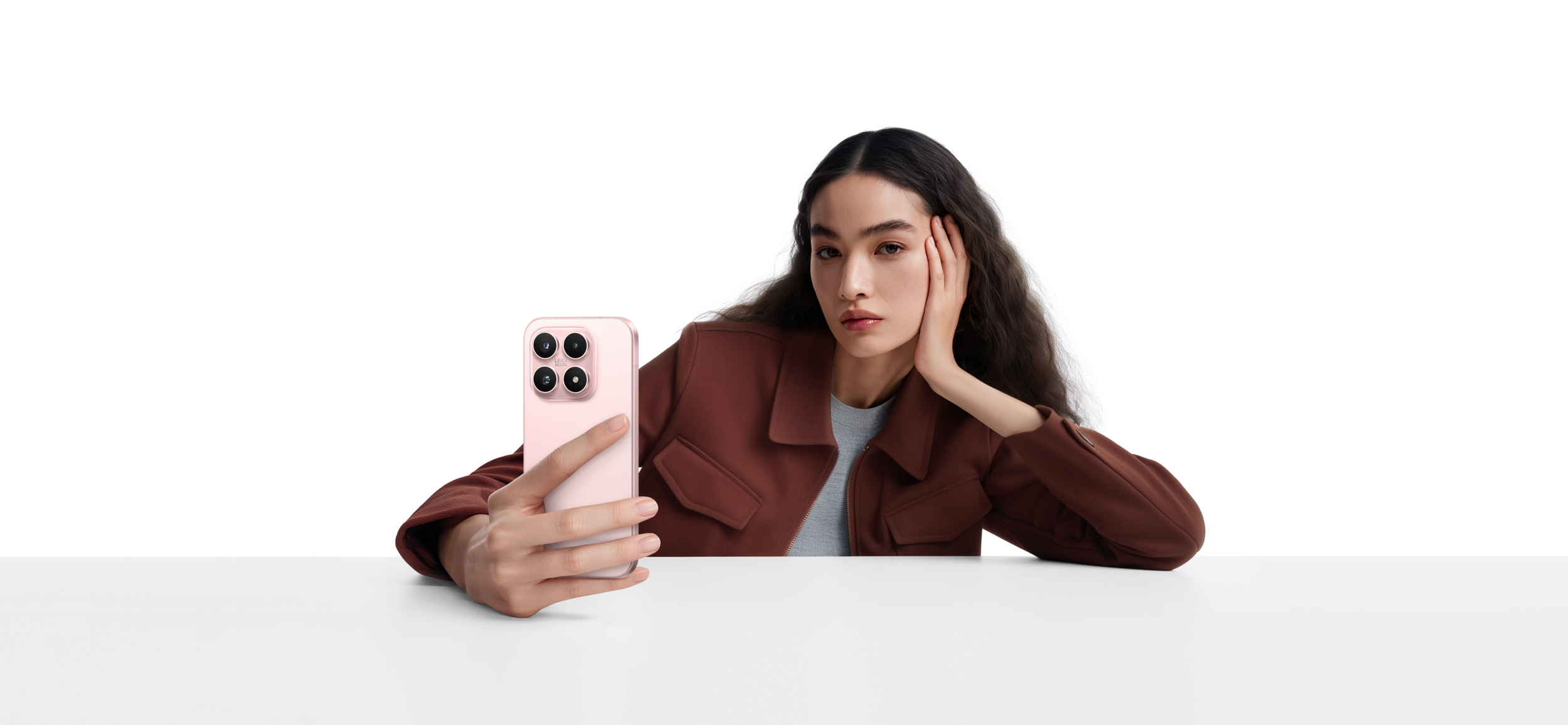 Una mujer de pelo largo y oscuro sostiene un teléfono inteligente rosa, sentada en una mesa.
