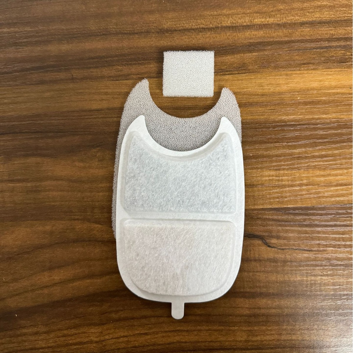 Tre filtri bianchi in schiuma e pile su un tavolo di legno.