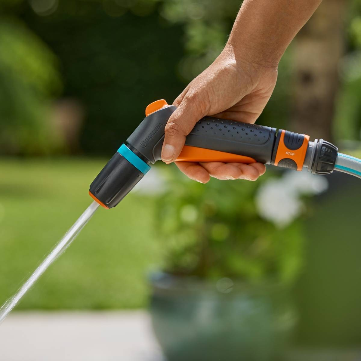 Mano che tiene un'irrigatore da giardino, getto d'acqua, sfondo verde giardino.