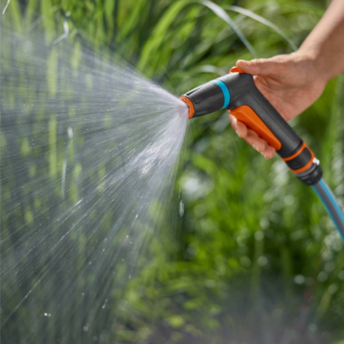 Mano che tiene una pistola a spruzzo, acqua che spruzza su fogliame verde.
