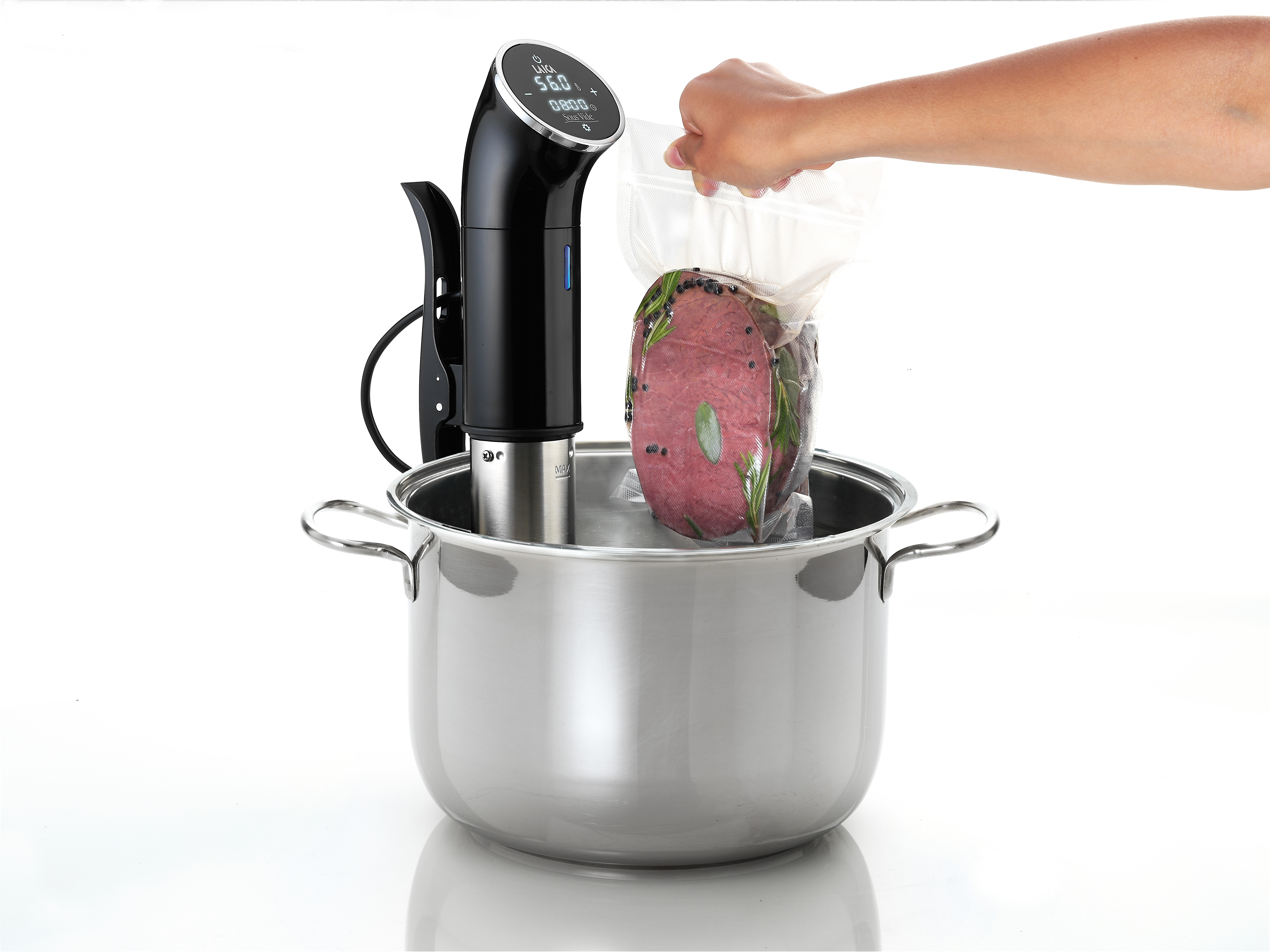 Un cocedor sous vide está en una olla con agua, una mano añade carne sellada al vacío.