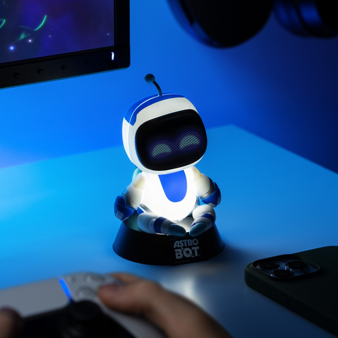 Mały świecący robot siedzi na biurku obok telefonu i kontrolera.