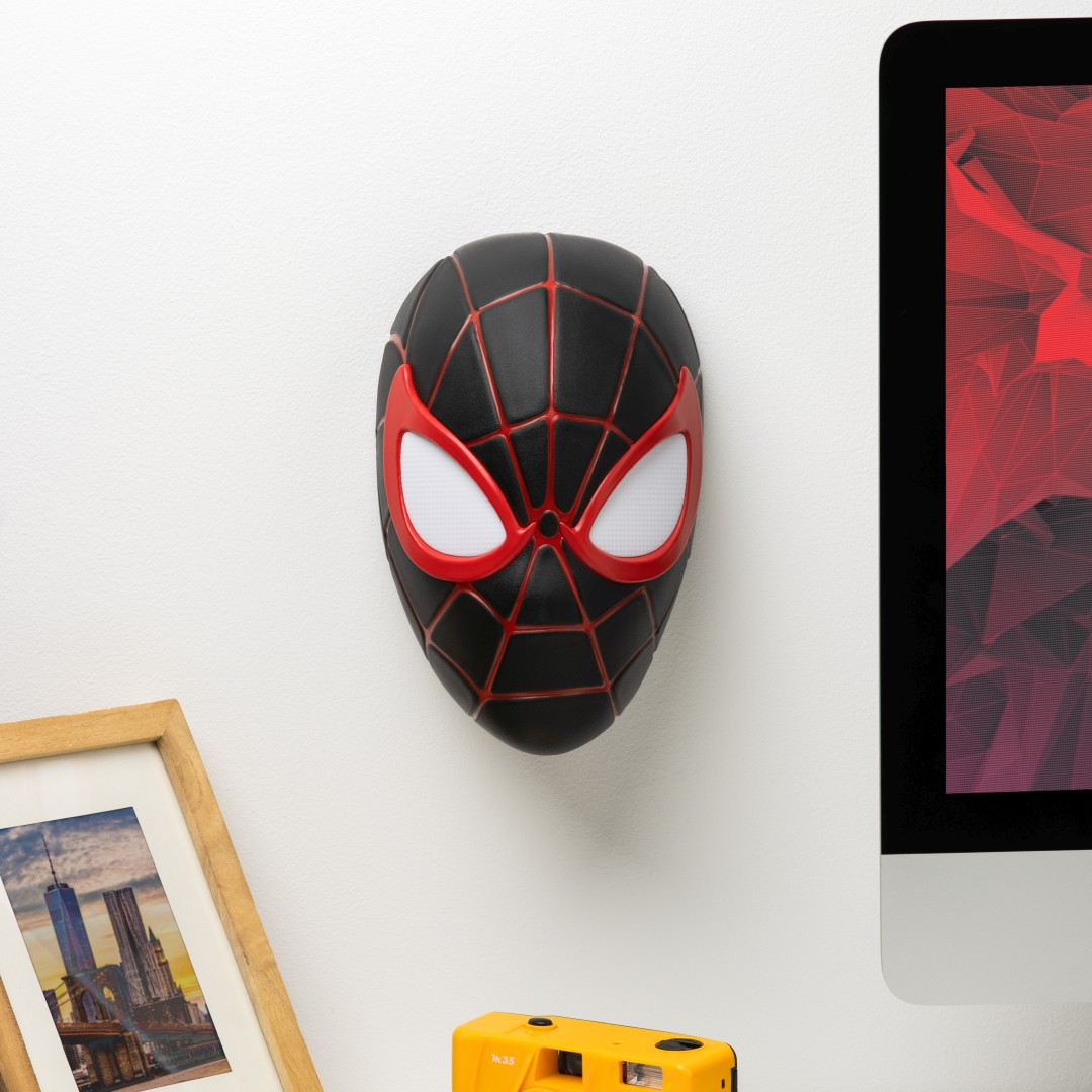 Czarna maska Spider-Mana z czerwonymi akcentami wisi na ścianie.