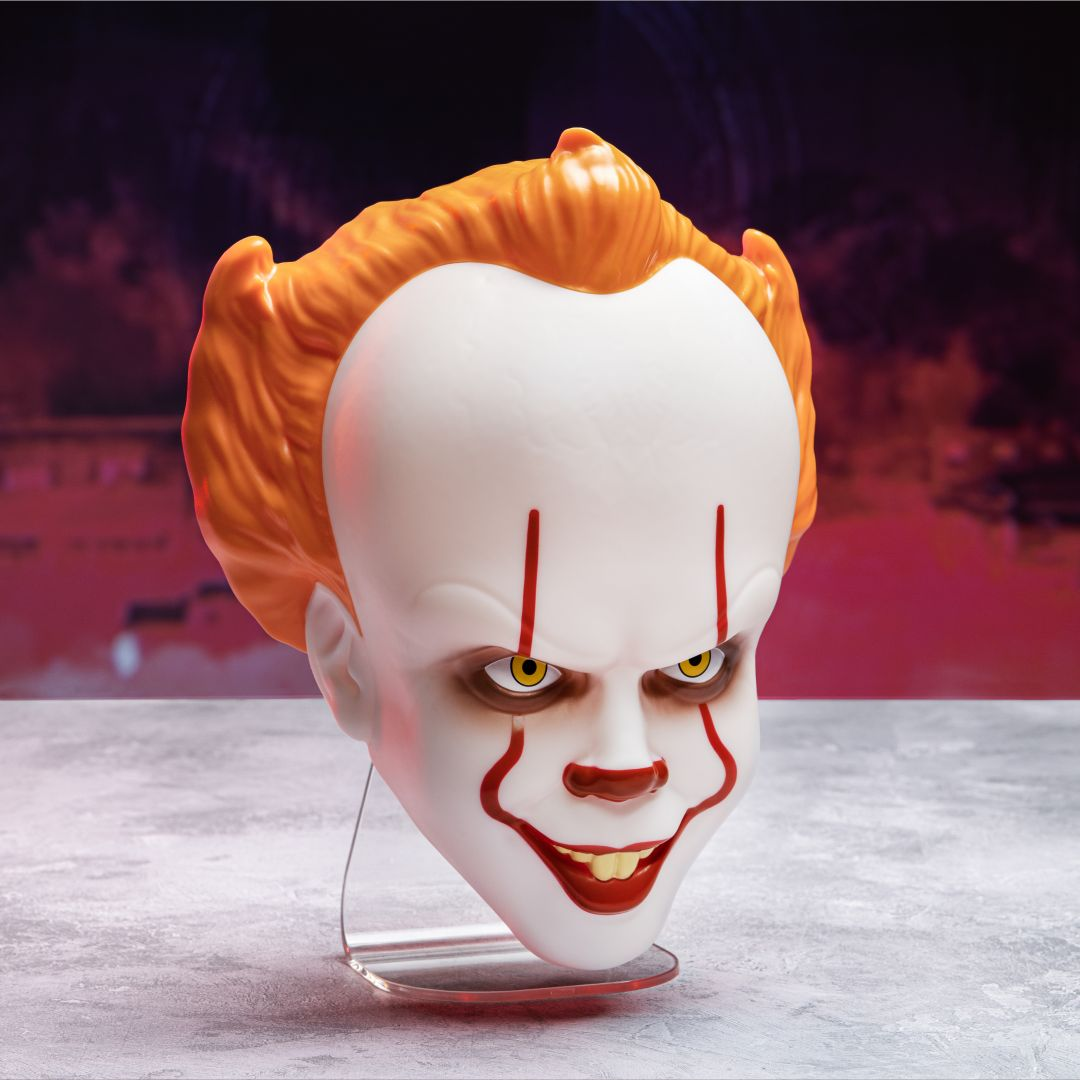 Maska Pennywise z pomarańczowymi włosami, żółtymi oczami i czerwoną twarzą na stojaku.