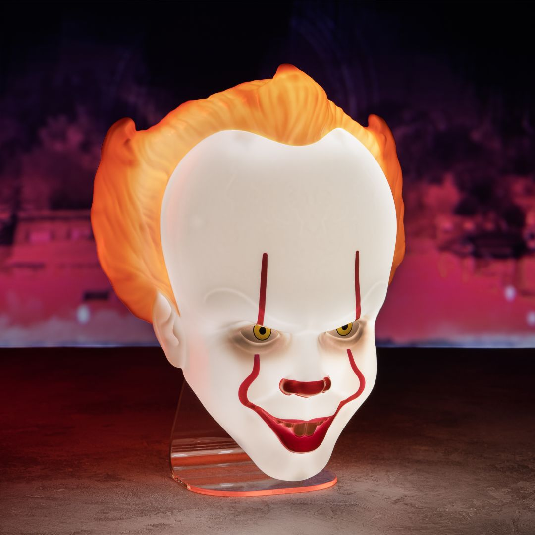 Lampa w kształcie głowy klauna Pennywise z pomarańczowymi włosami i świecącą białą twarzą.