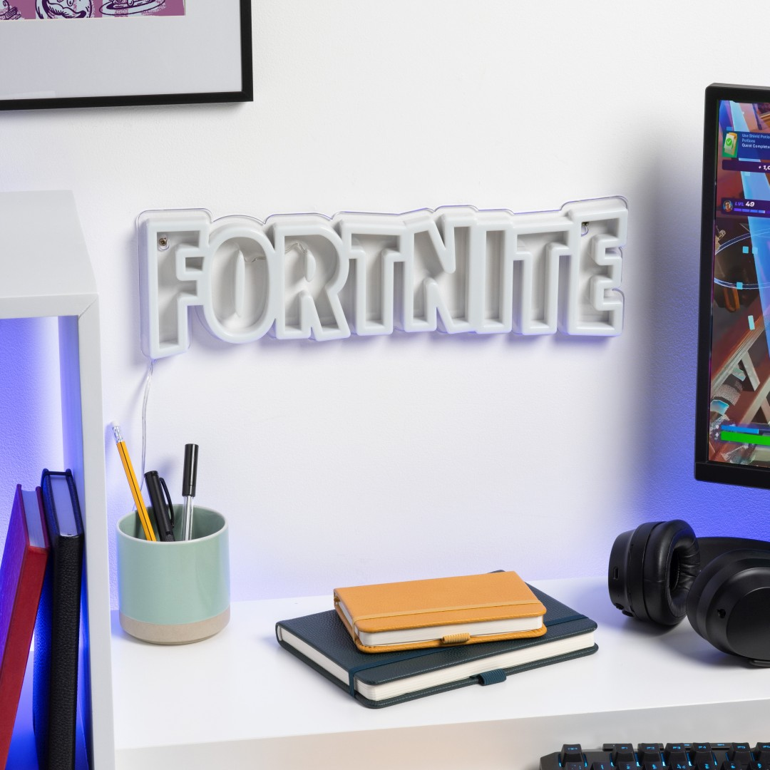 Białe logo Fortnite świeci na ścianie nad biurkiem z notatnikami i długopisami.
