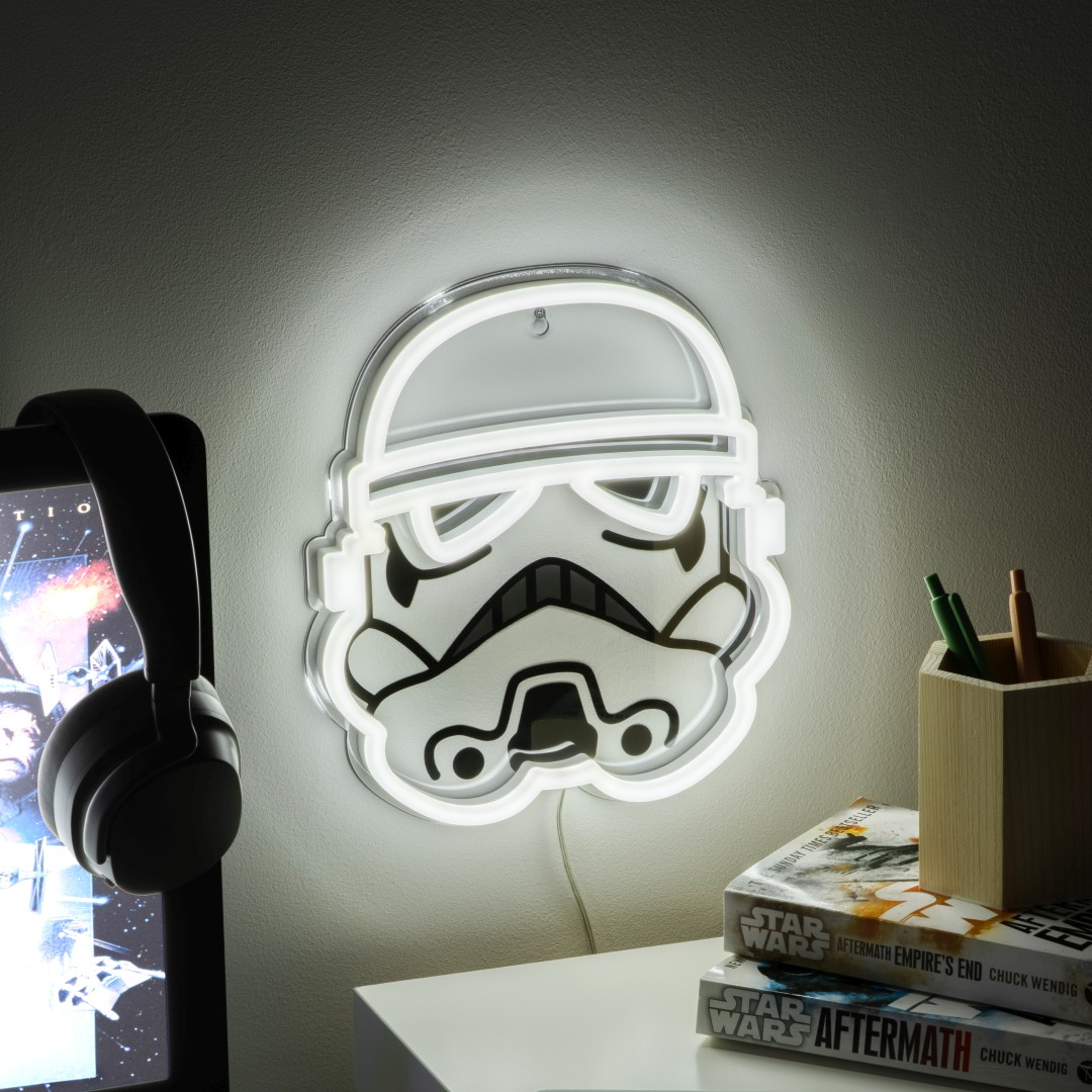 Neonowe światło Star Wars Stormtrooper świeci nad biurkiem z książkami.