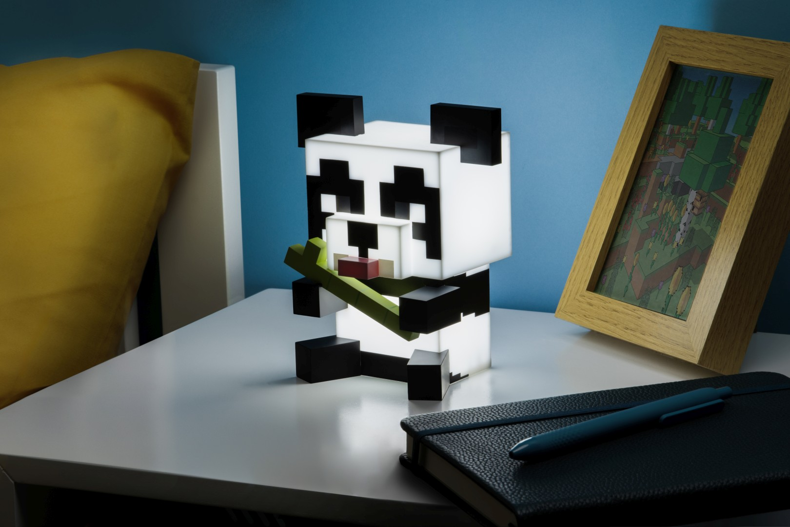 Lampa panda pixelowa trzyma bambus na stoliku nocnym obok ramki na zdjęcia.