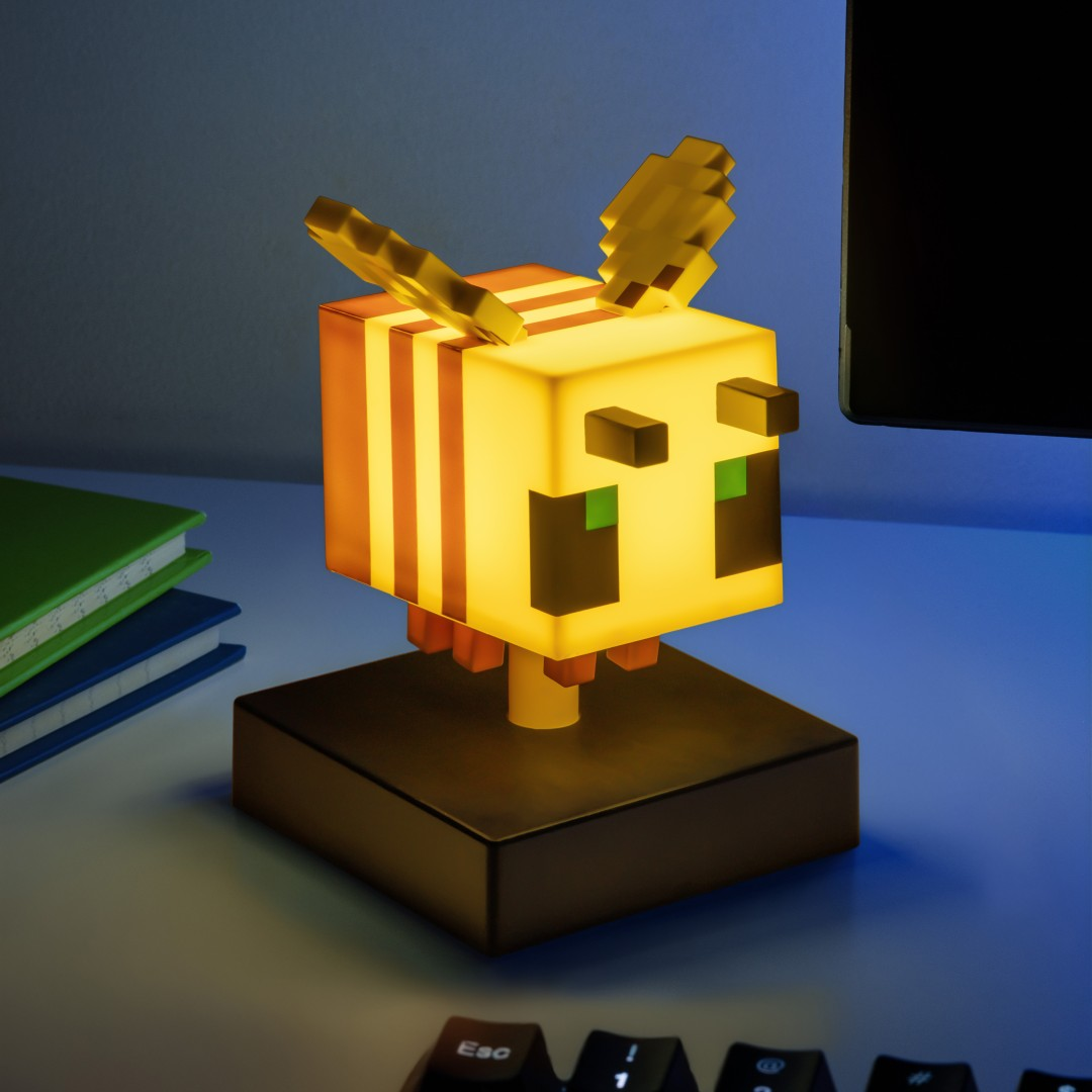 Świecąca lampa pszczoła z Minecrafta stoi na biurku obok książek i klawiatury.