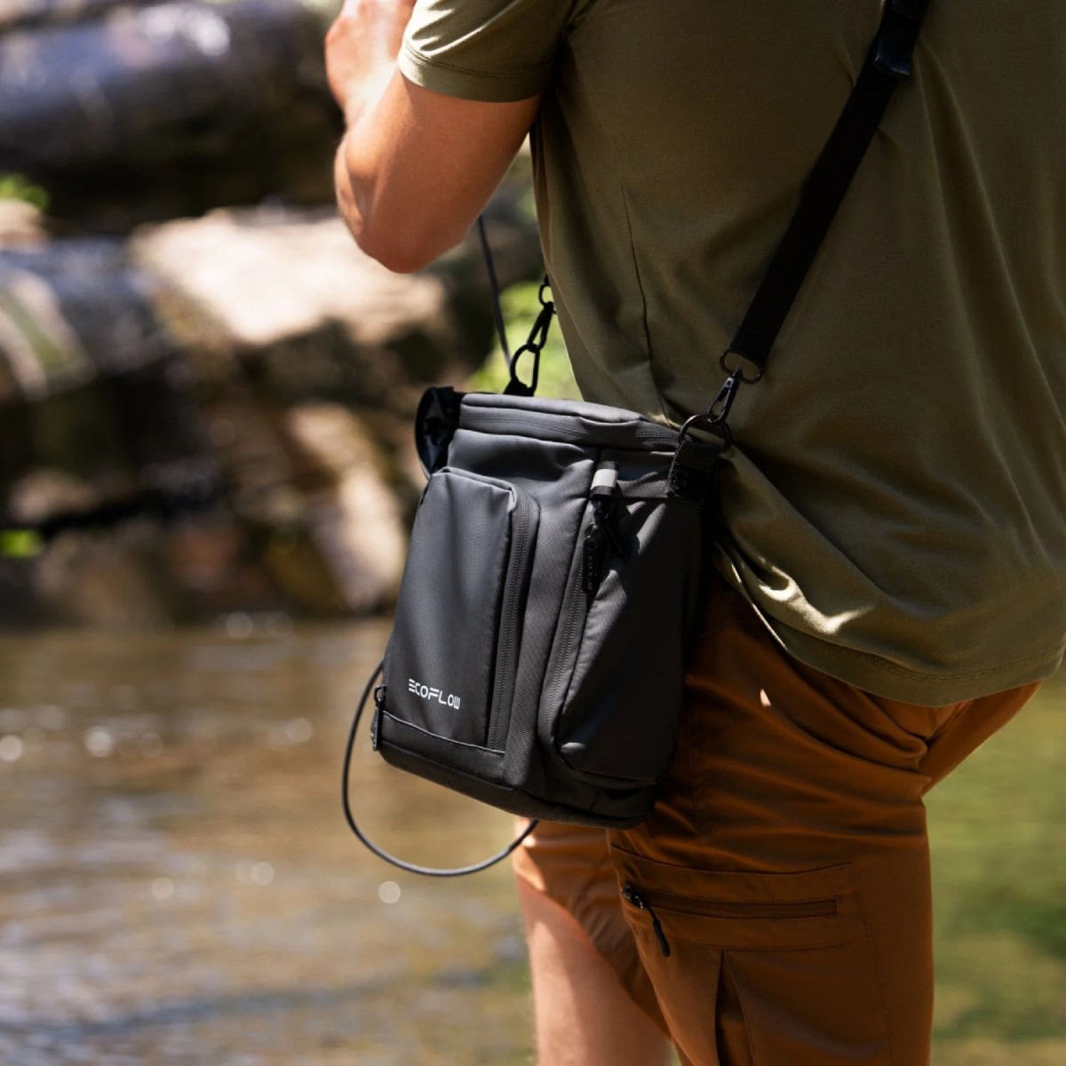 Una persona indossa una borsa nera ECOFLOW e pantaloncini marroni vicino a un ruscello.