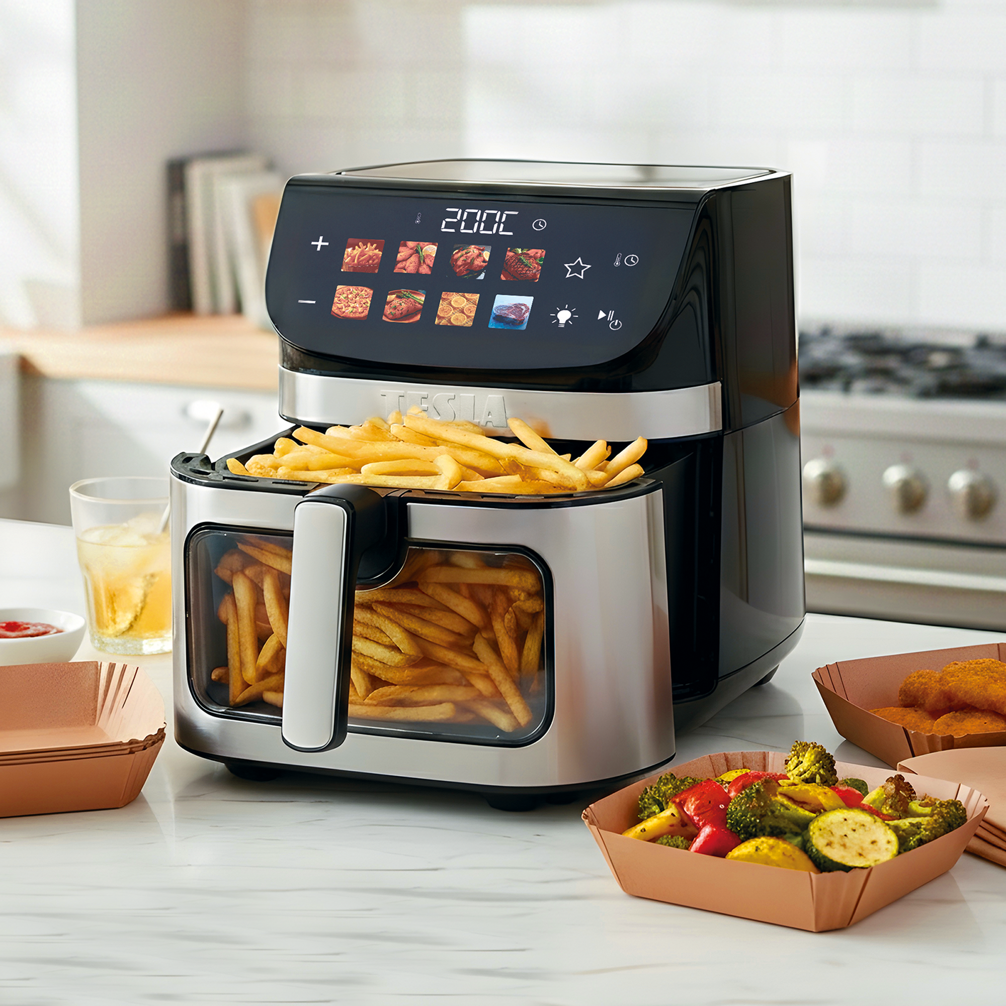 Una friggitrice ad aria nera piena di patatine fritte, accanto a verdure arrosto e nuggets.