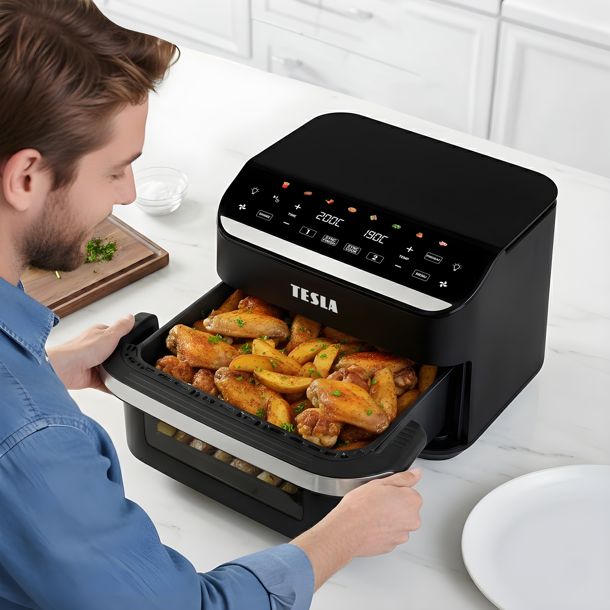 Uomo estrae un cassetto di ali di pollo e patate da una friggitrice ad aria nera.