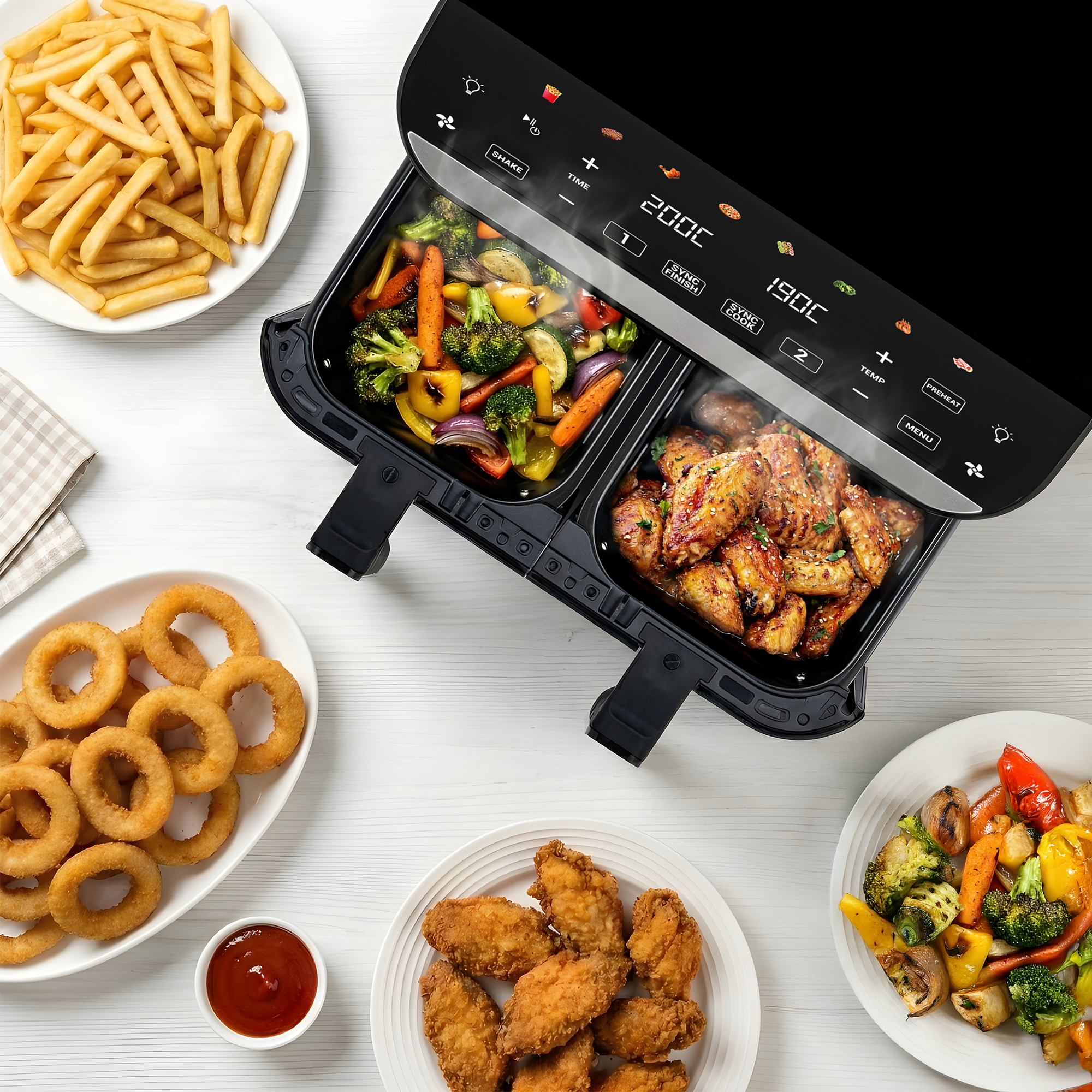 Friggitrice ad aria doppia con verdure e alette di pollo, patatine e anelli di cipolla accanto.
