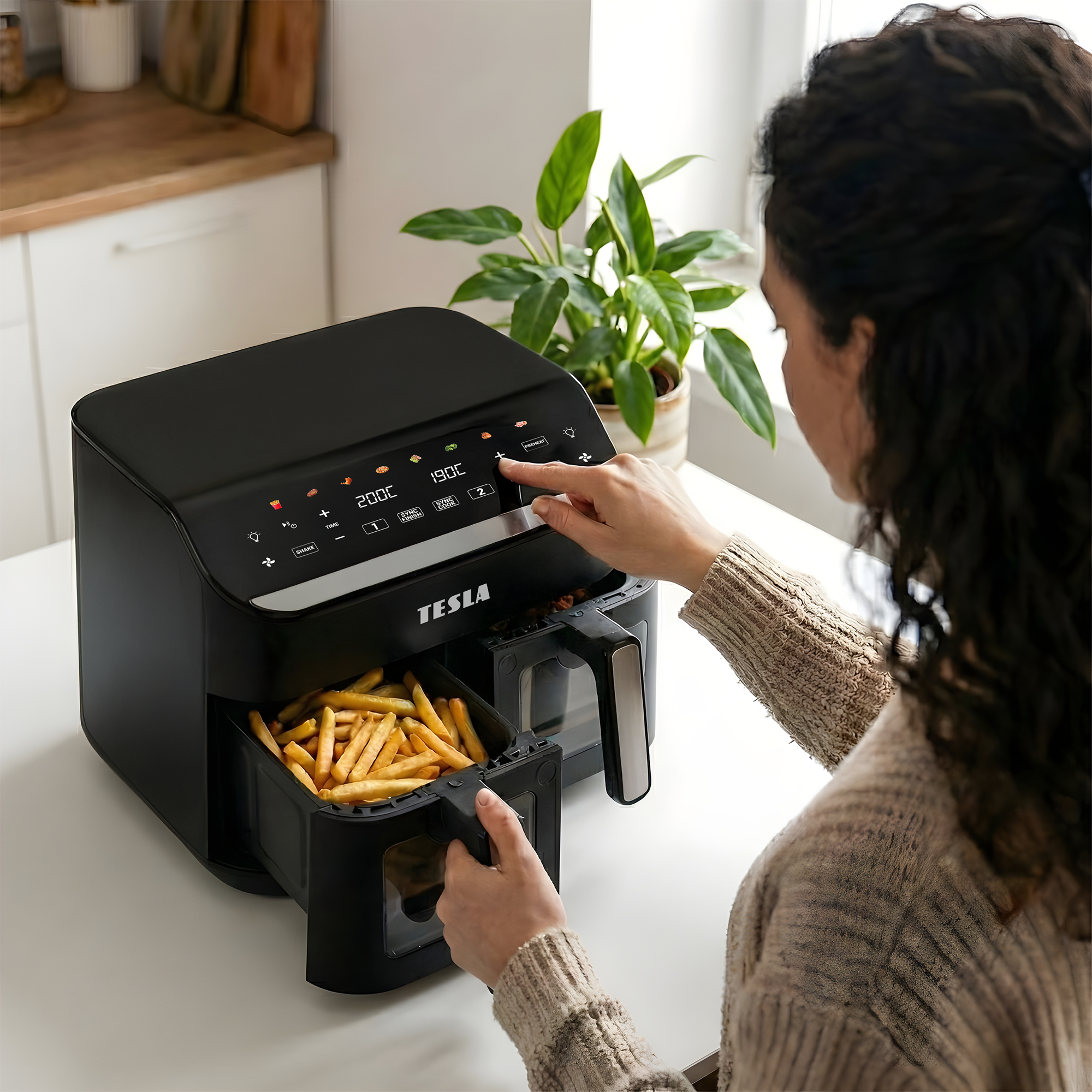 Una donna aziona una friggitrice ad aria nera con patatine fritte.