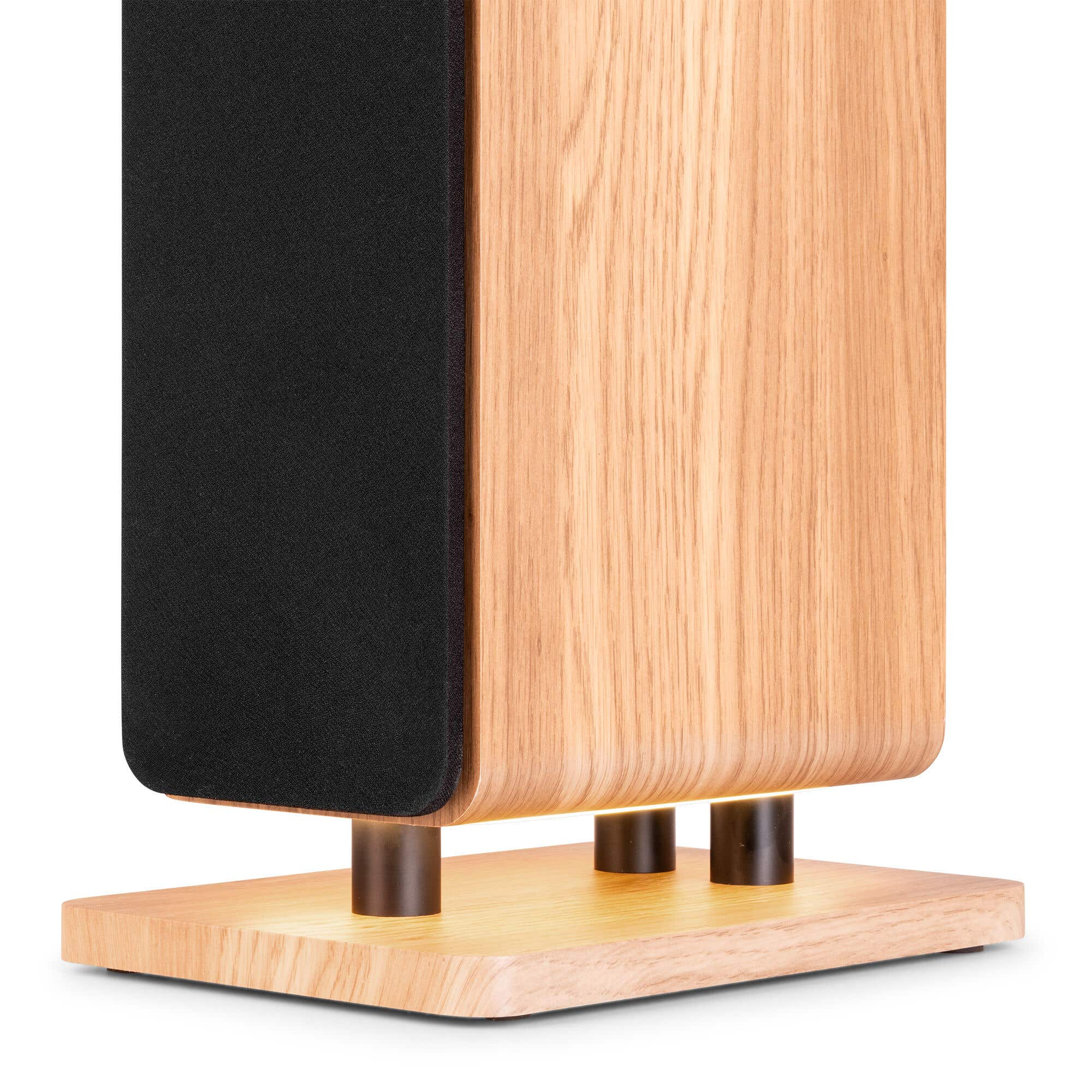 Un altavoz de madera con rejilla de tela negra se apoya en una base de madera con pies metálicos.